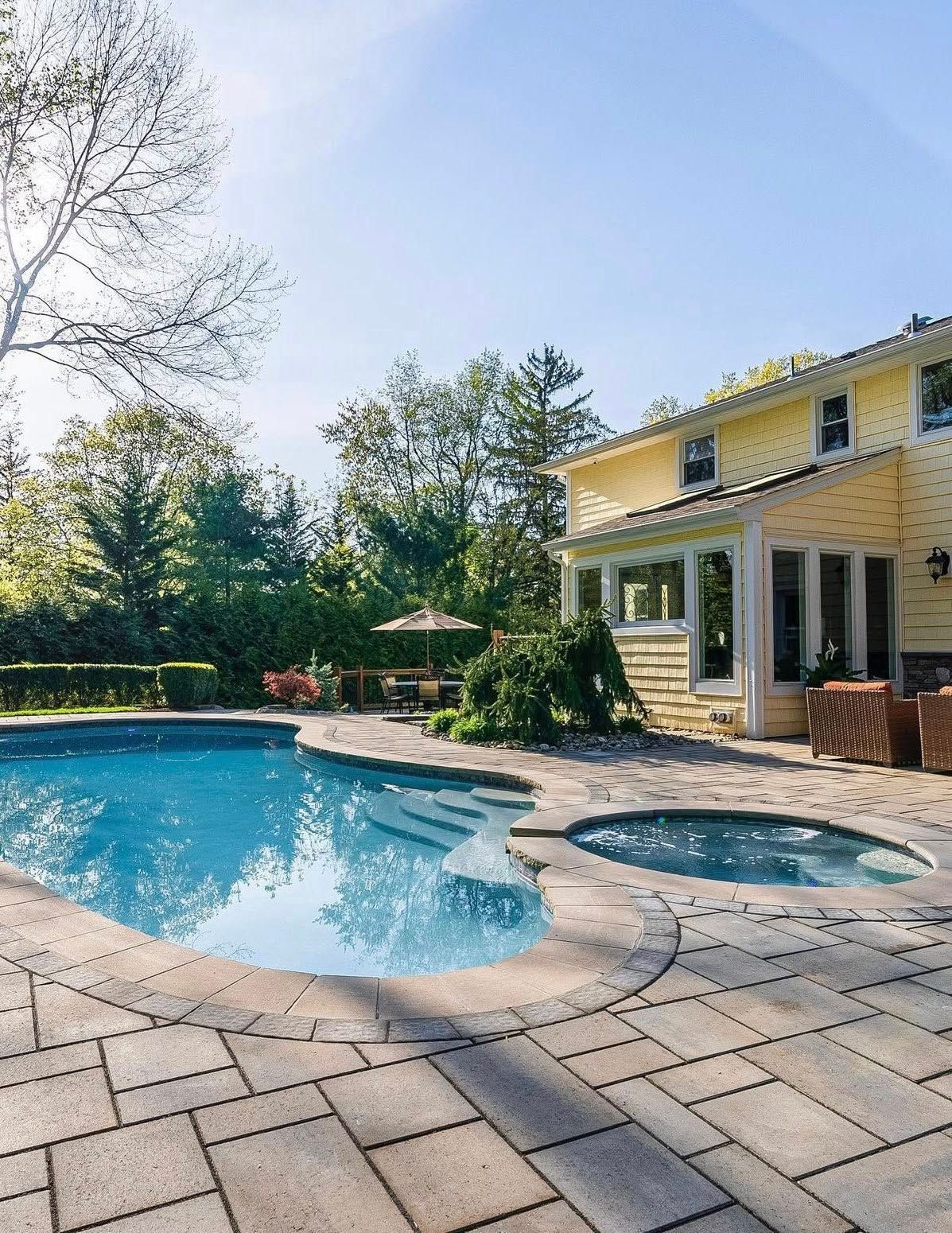 Backyard with a swimming pool, spa, yellow house, and patio on a sunny day.
