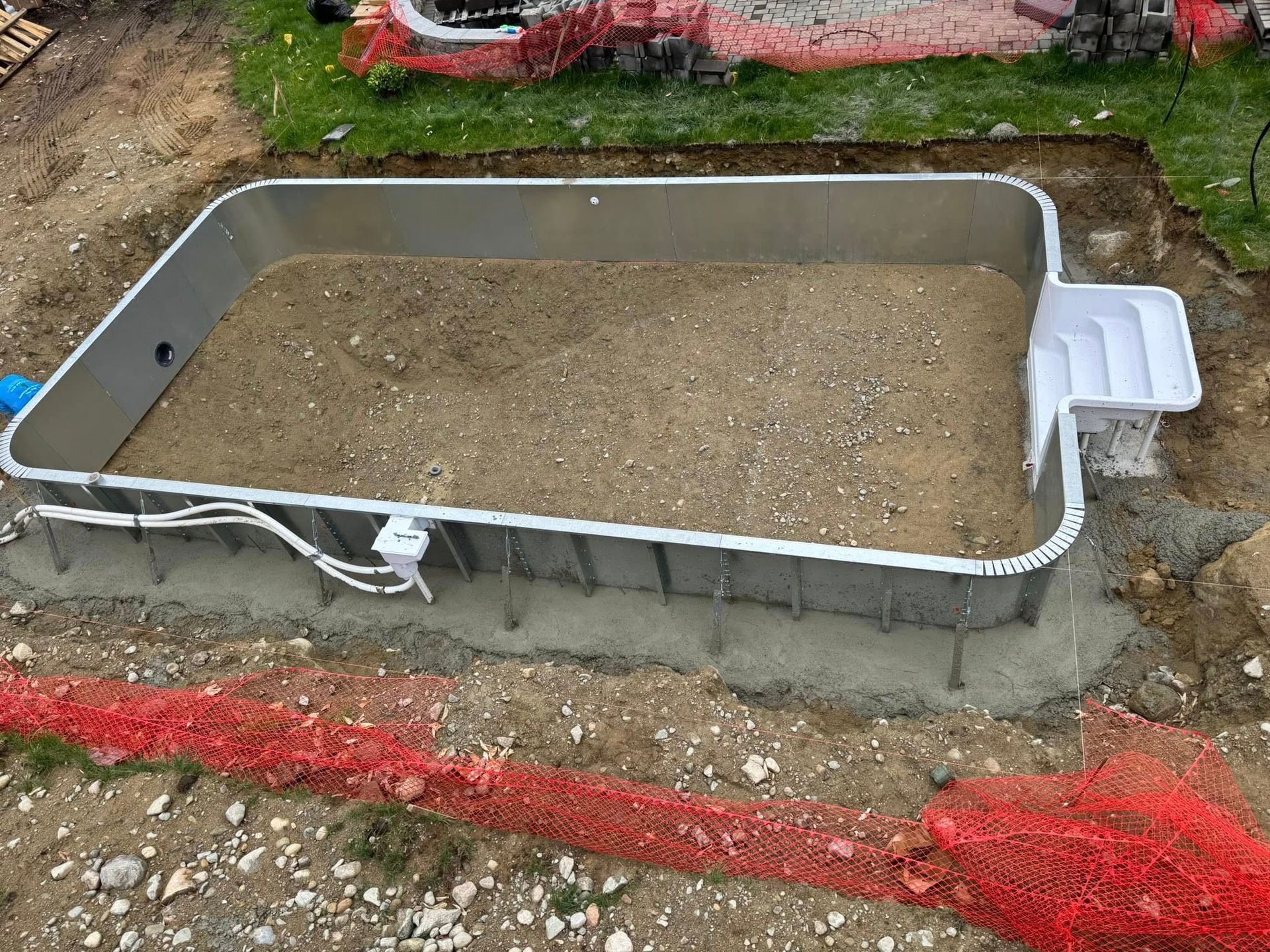 Above-ground rectangular pool under construction, metal frame with sand base, next to a white stair section.