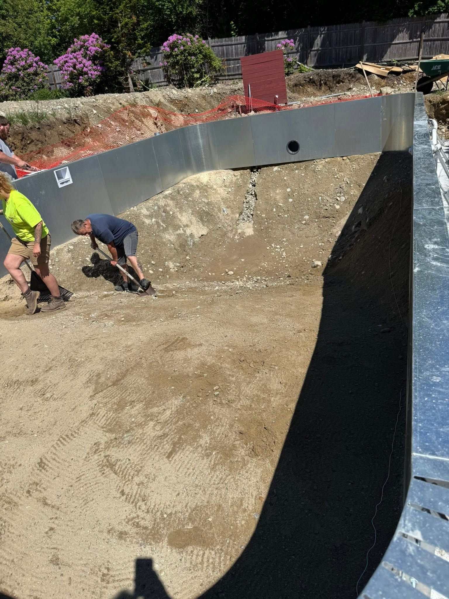 Construction workers leveling gravel in a pool frame.