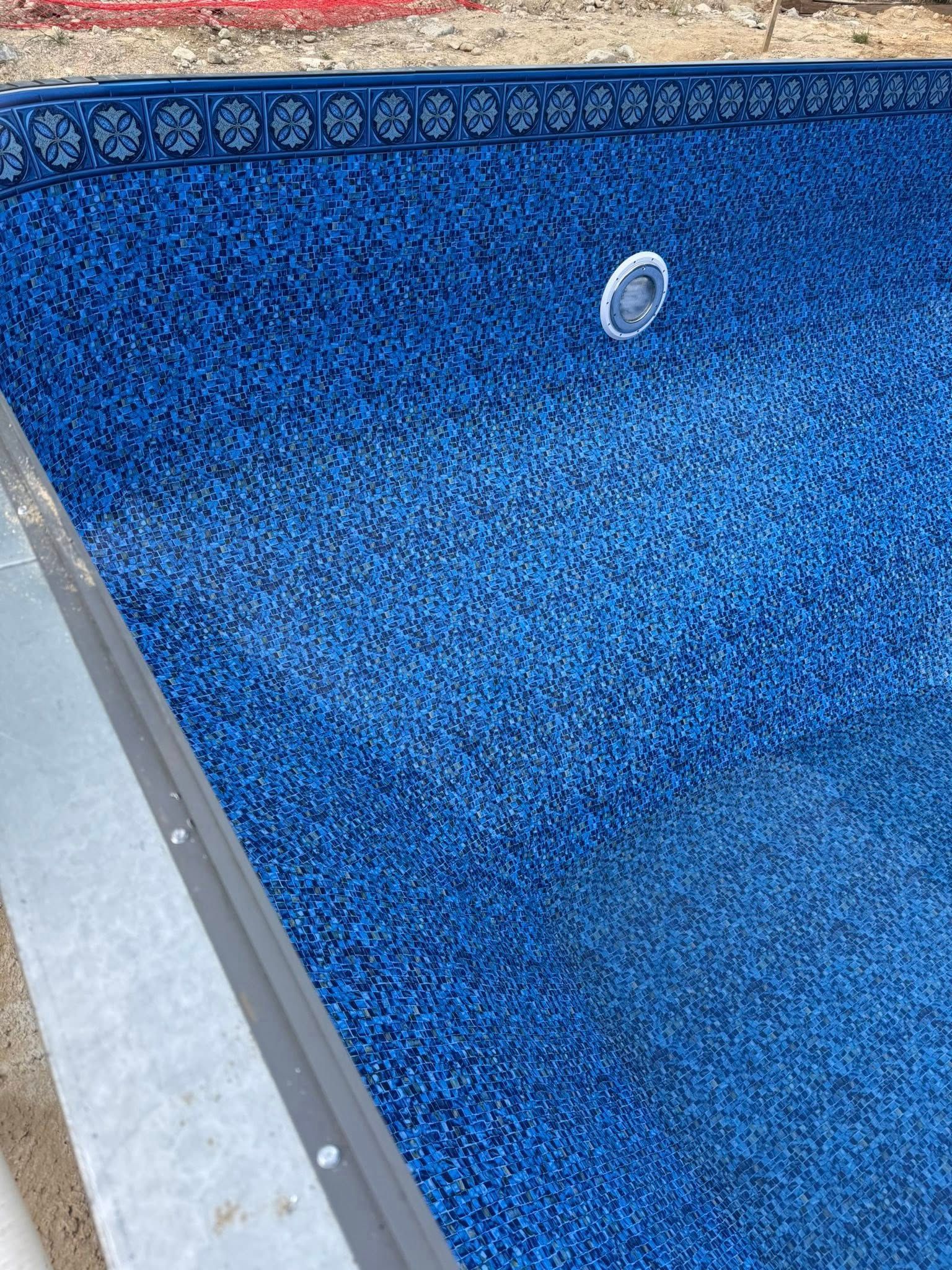 Blue mosaic-tiled pool interior with water, surrounded by gray edging.