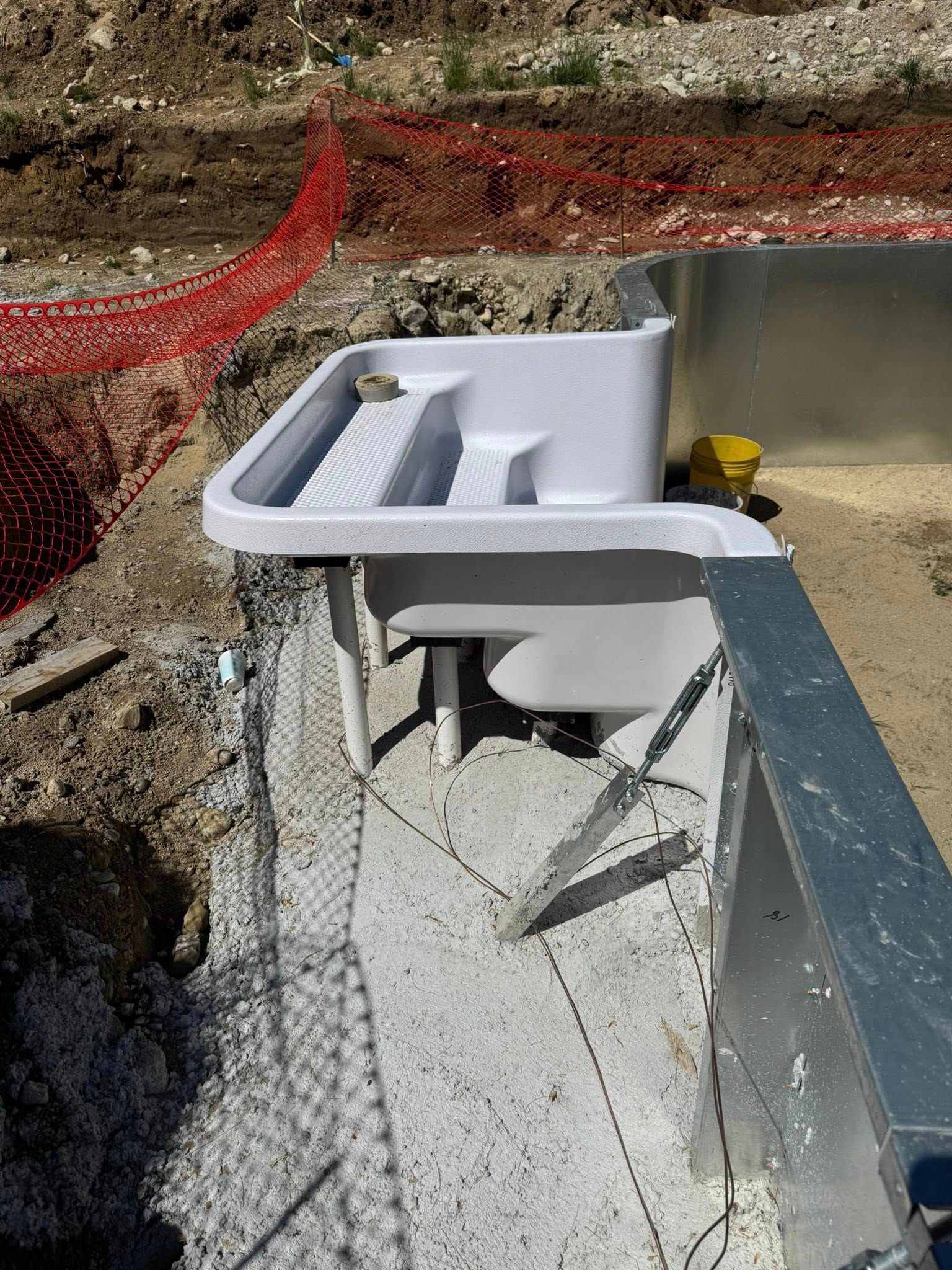 White in-pool tanning ledge and steps under construction near pool edge, orange safety netting in background.