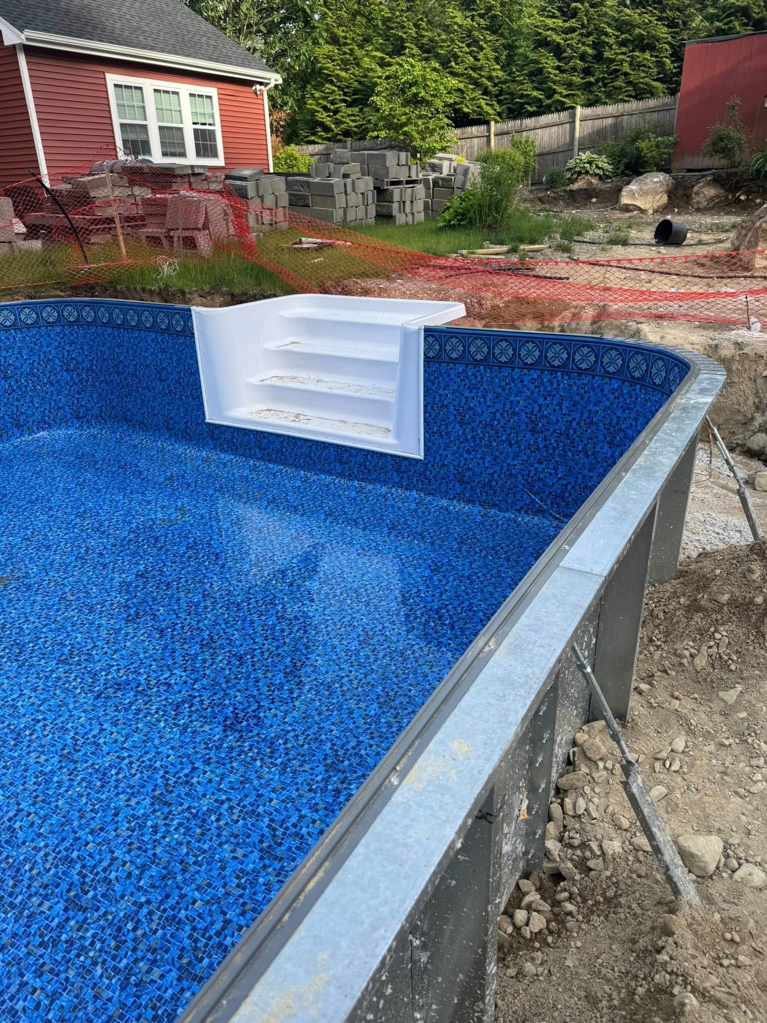 Pool under construction with blue interior, white steps, and red building in the background.