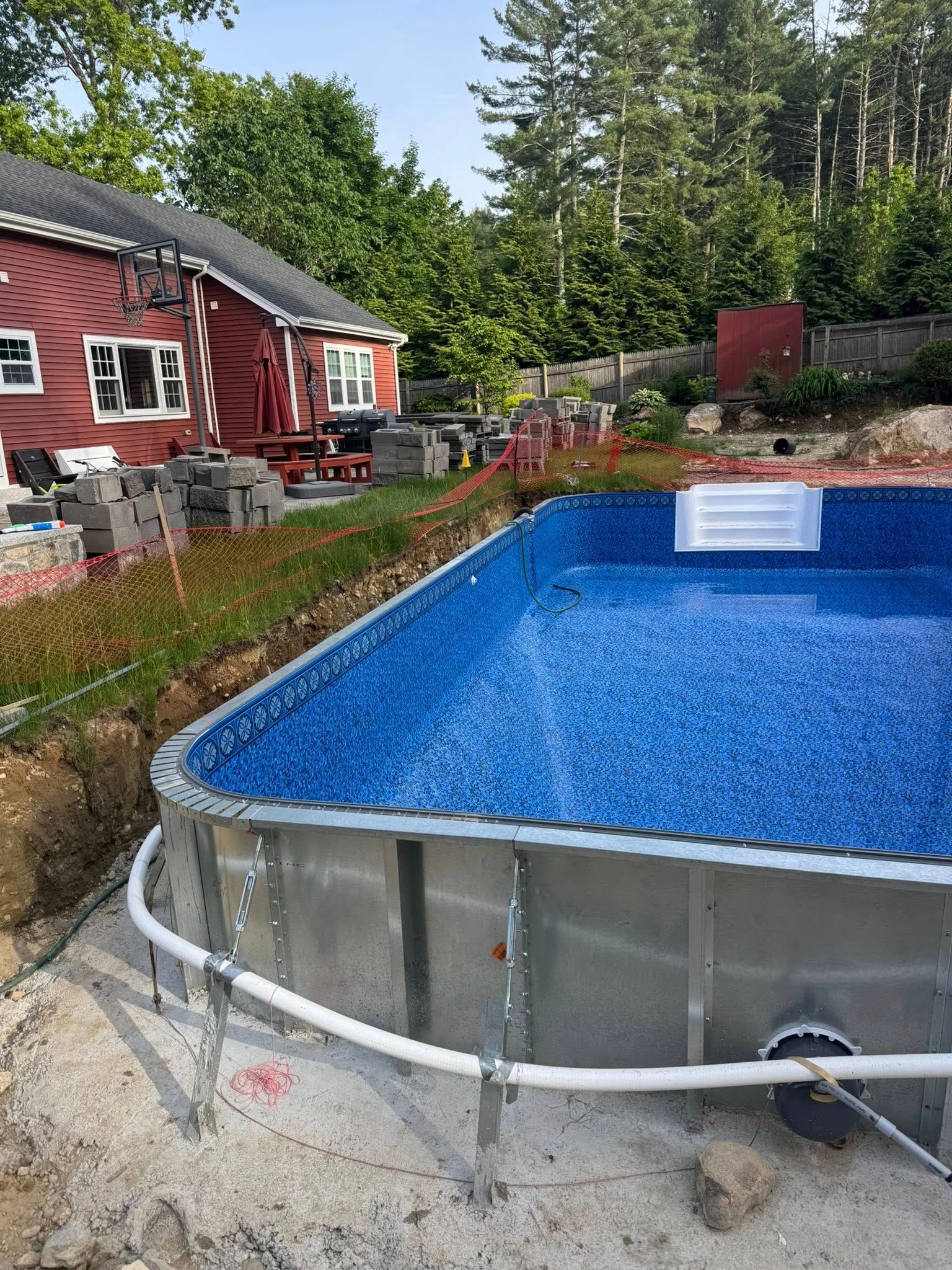 Pool under construction next to a red house. Steel frame and blue liner are visible.