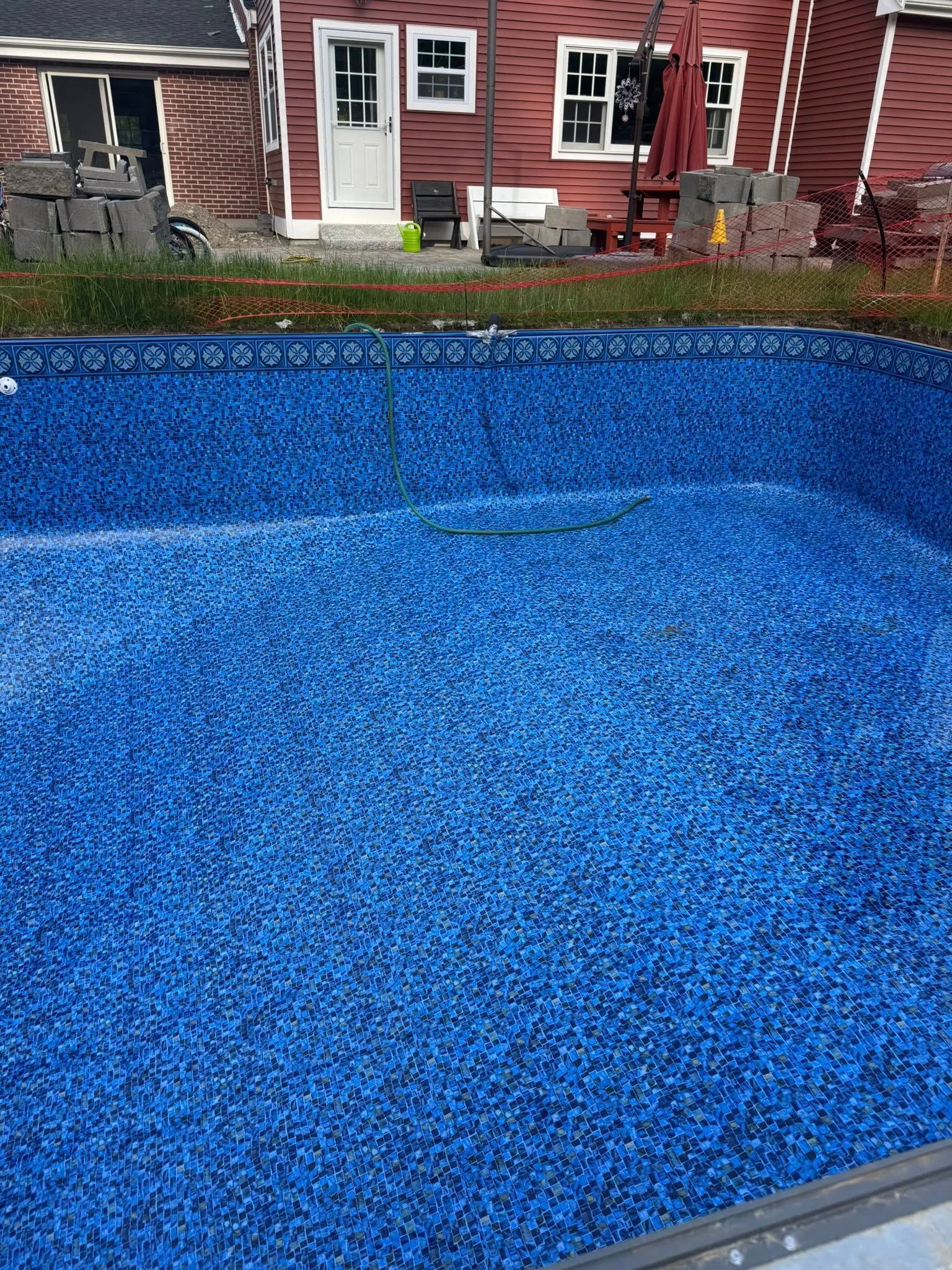 Blue-patterned pool interior. Red house in the background. Construction materials are visible near the house.
