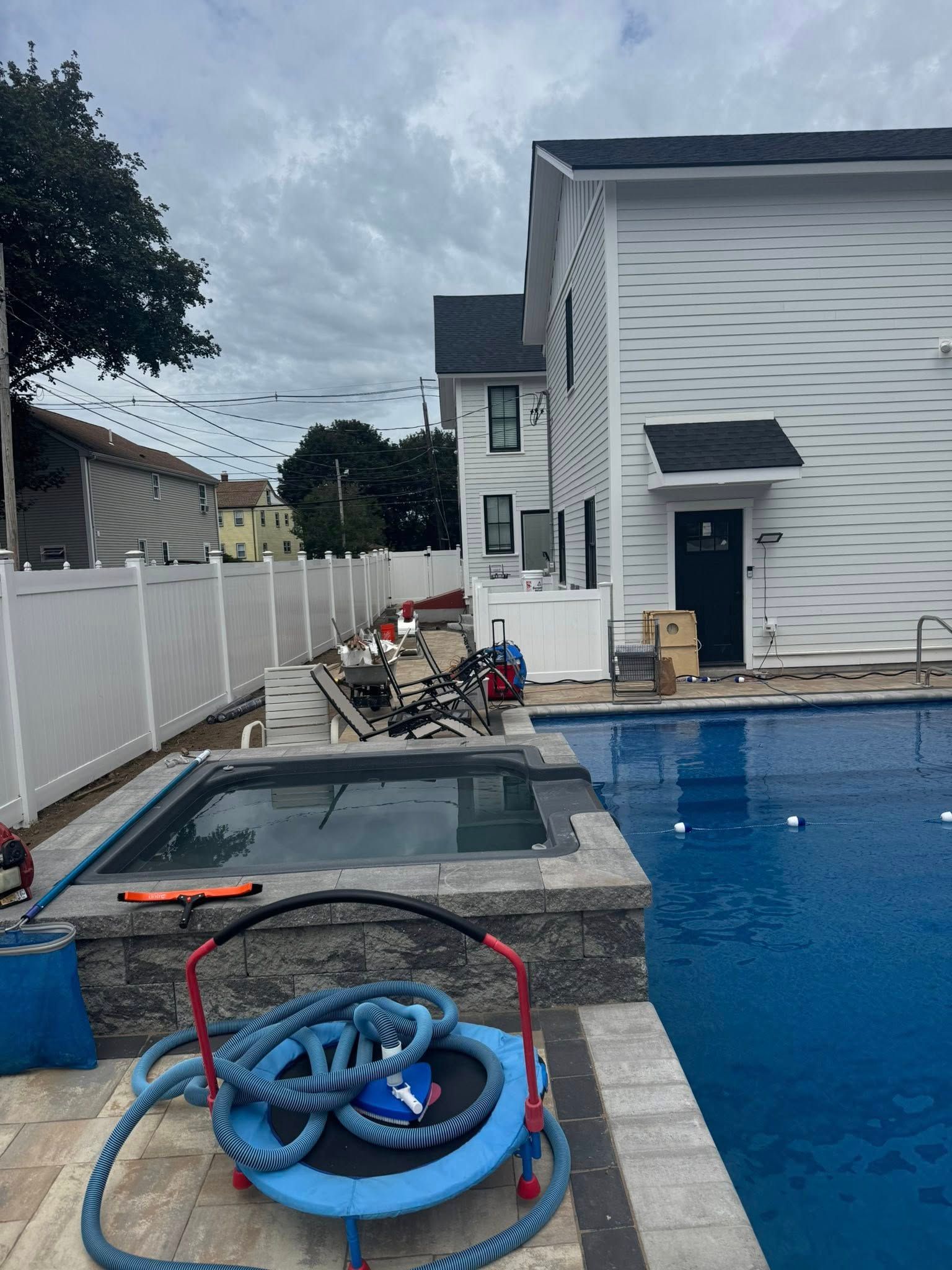 Pool area with jacuzzi under construction, white fence, building, and cloudy sky.