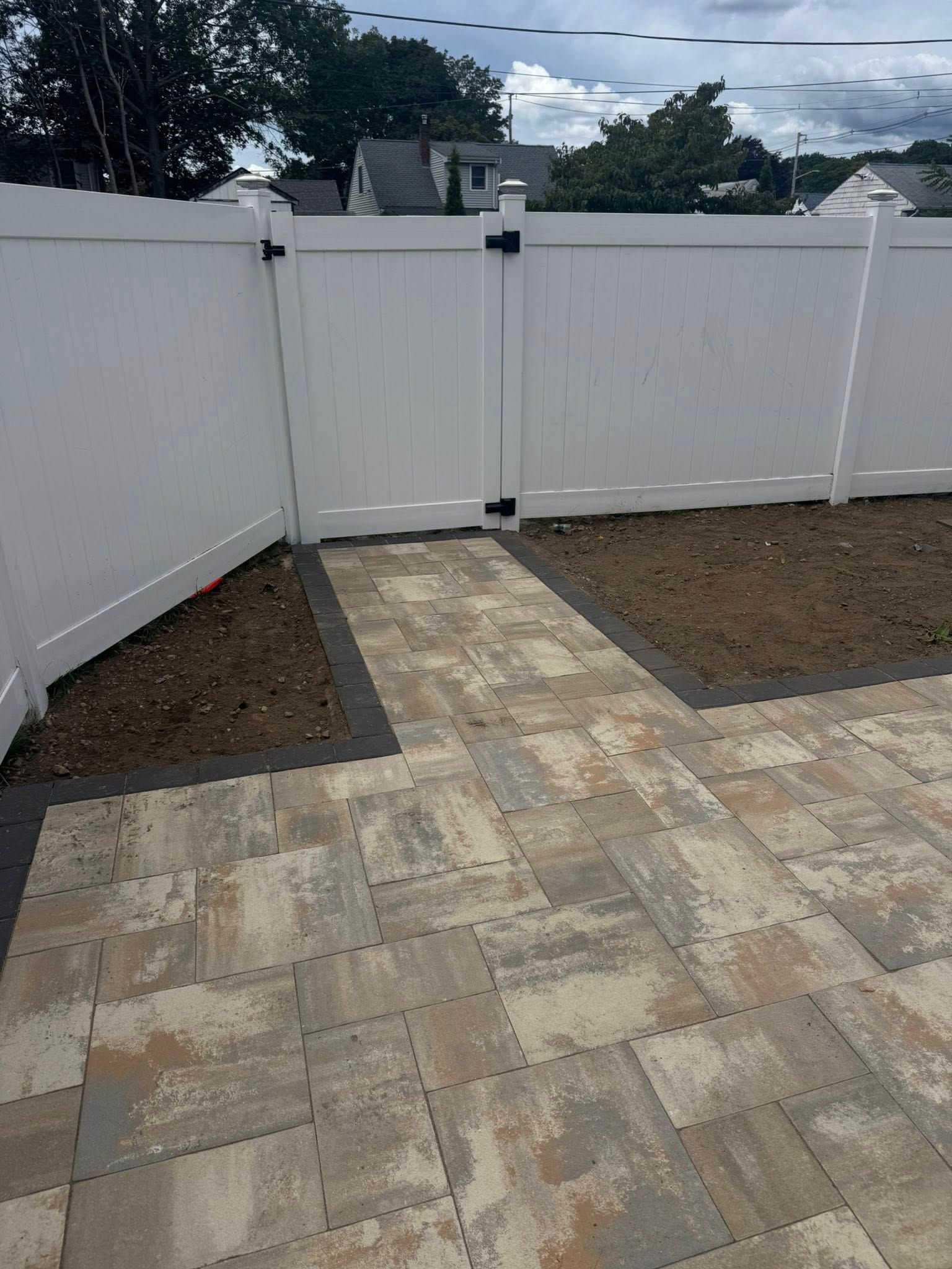 White vinyl fence with gate, leading to a paved patio. Garden beds border the walkway.
