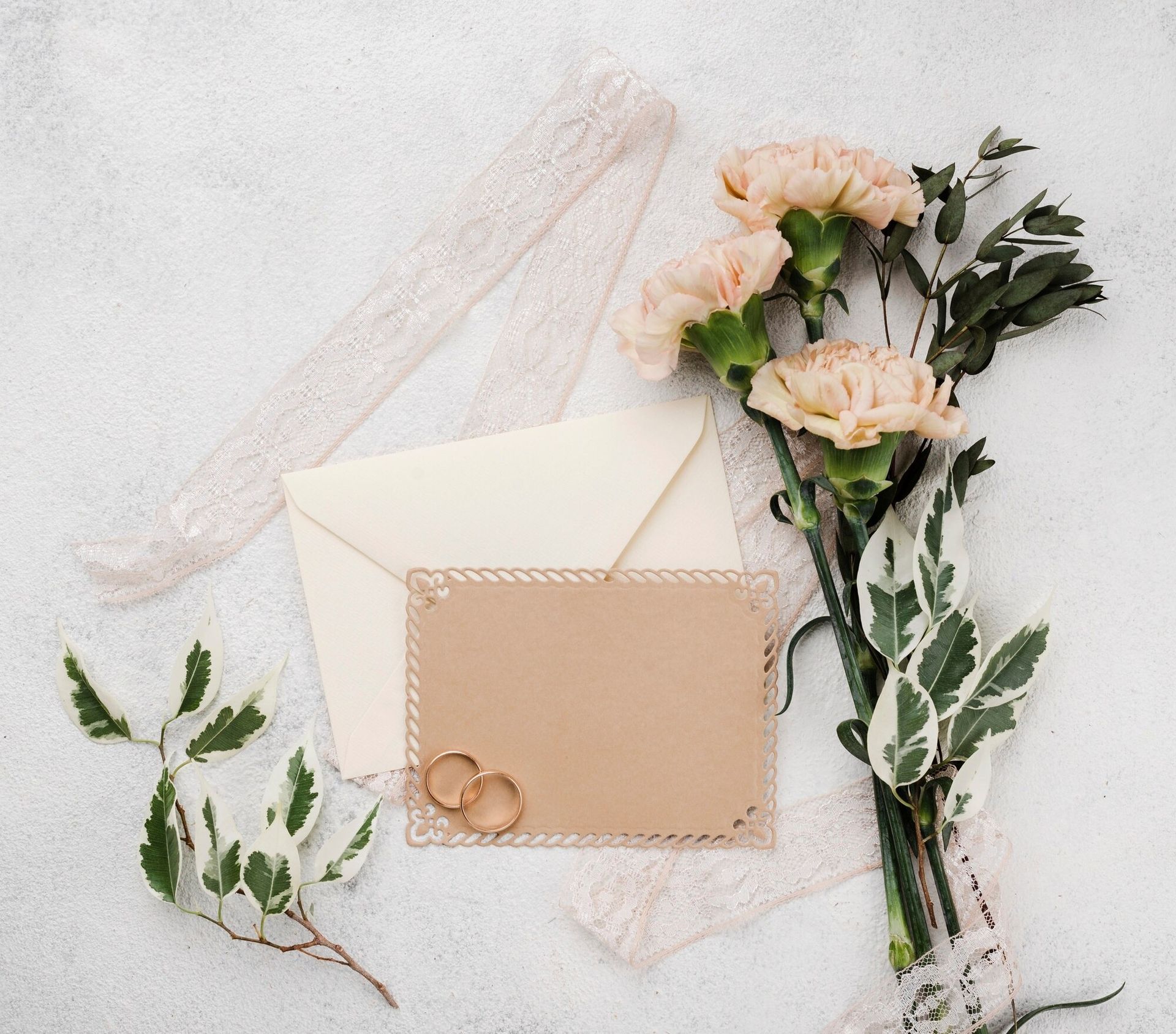 Wedding stationary with rings, flowers, and lace on a white background.