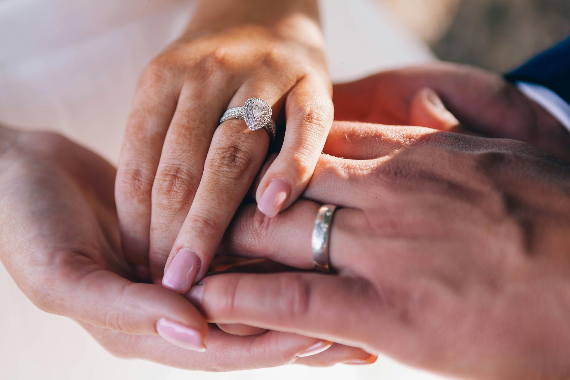 Hands clasped, showing wedding rings. Diamond engagement ring, silver band.