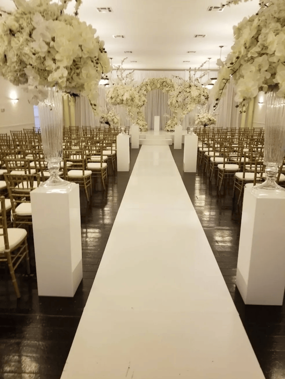 Wedding ceremony setup: white aisle, rows of chairs, floral arch, and decorations.