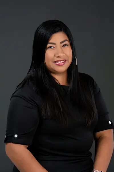 Woman with dark hair, wearing a black top, smiling against a gray backdrop.