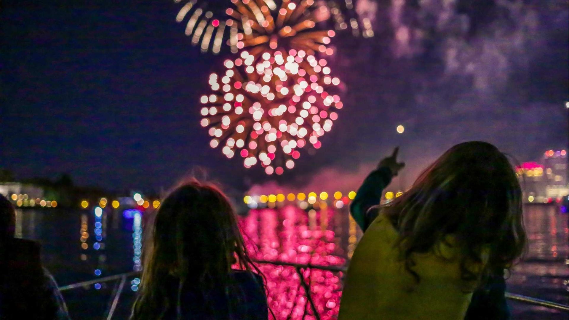 two little girls watching fireworks from a boat in the harbor