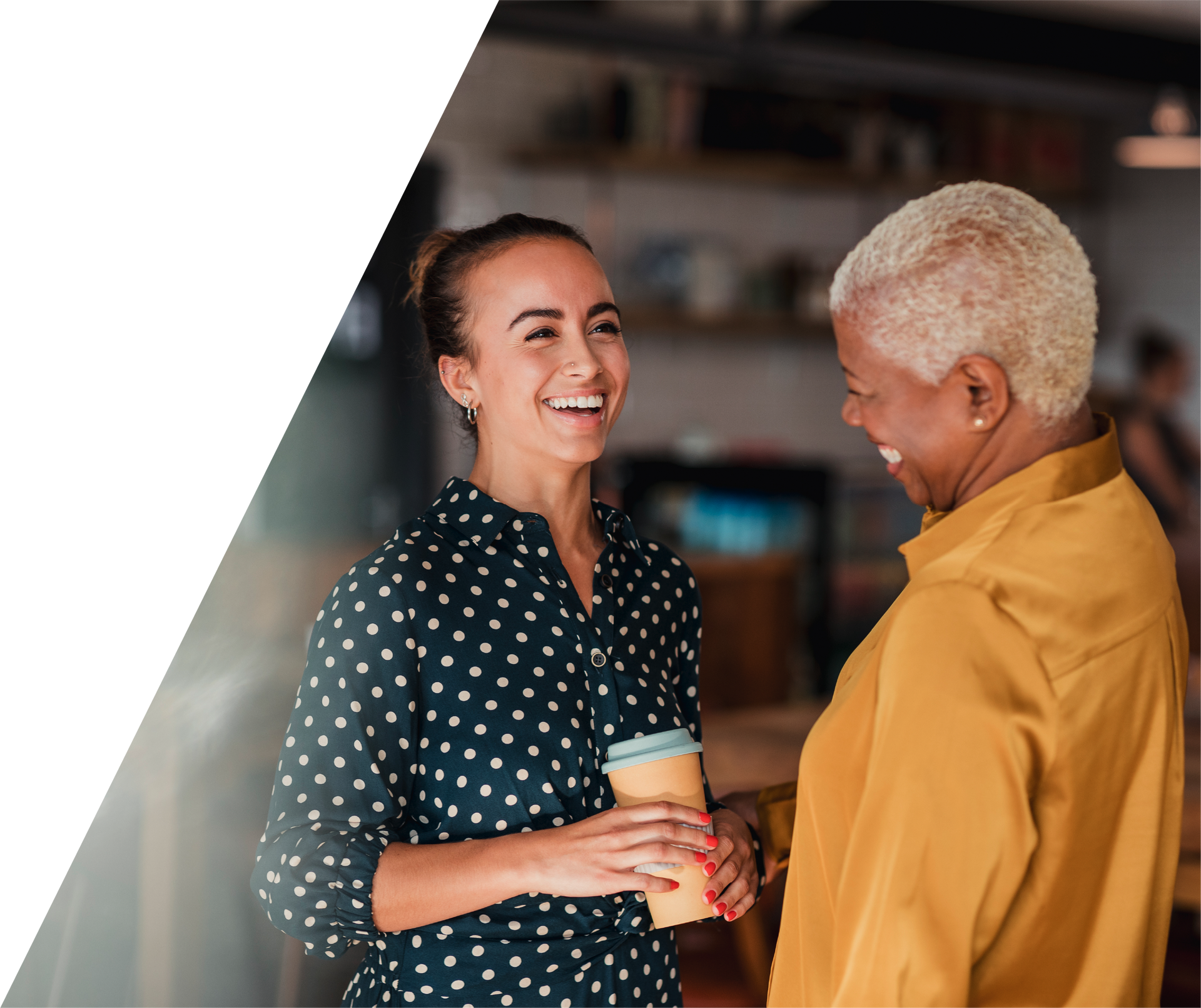 Two women are standing next to each other holding cups of coffee and smiling.