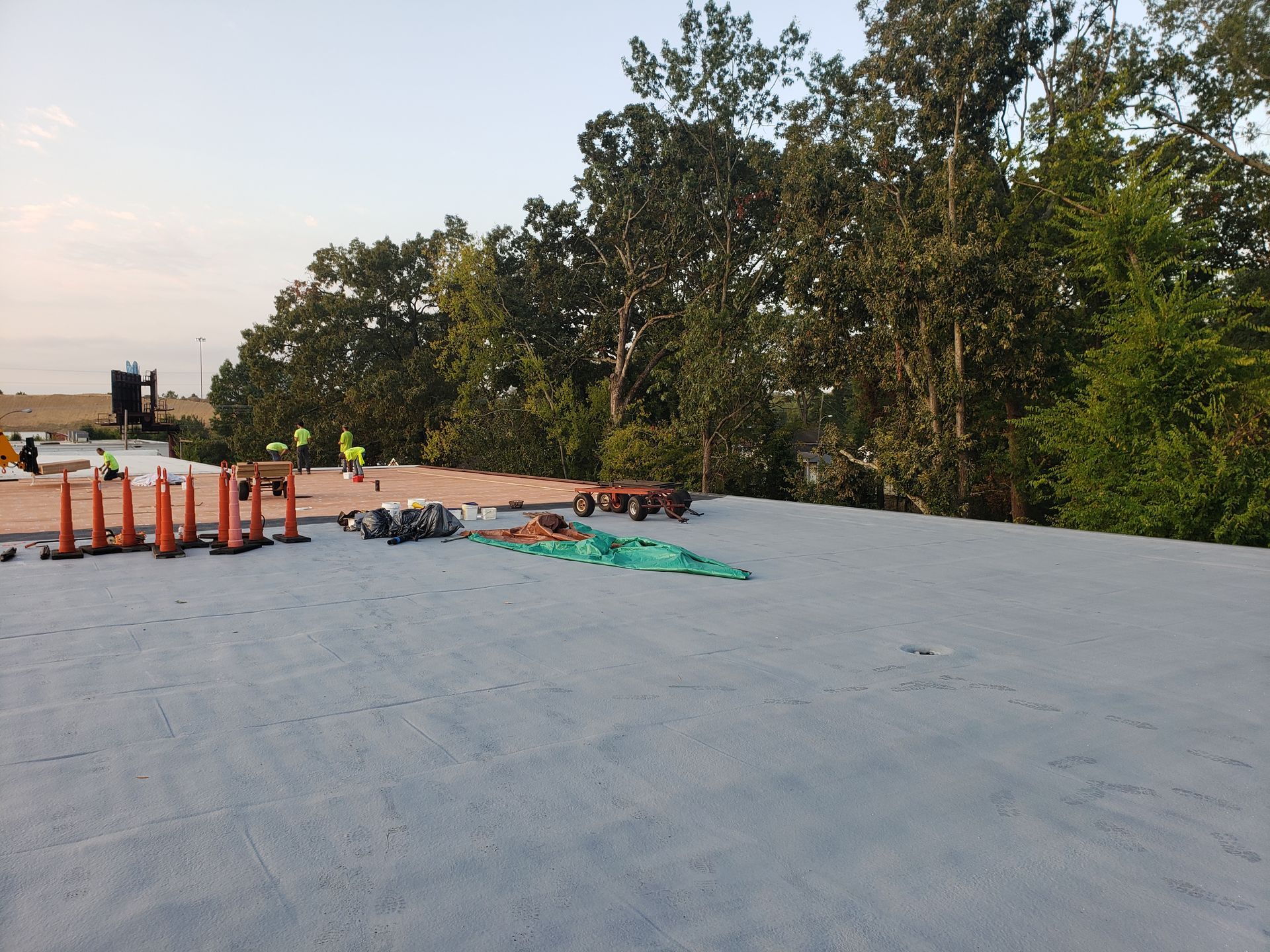 A group of construction workers are working on a roof with trees in the background.