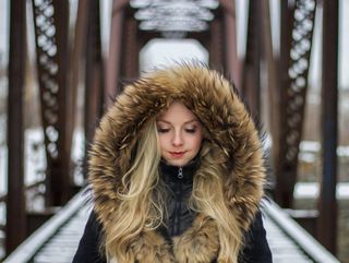 A woman wearing a fur hooded jacket is standing on a bridge.