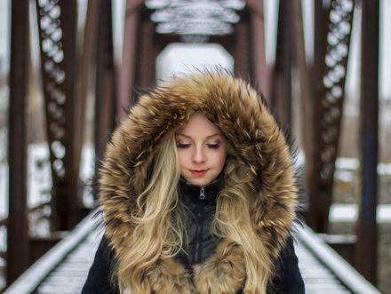 A woman wearing a fur hooded jacket is standing on a bridge.