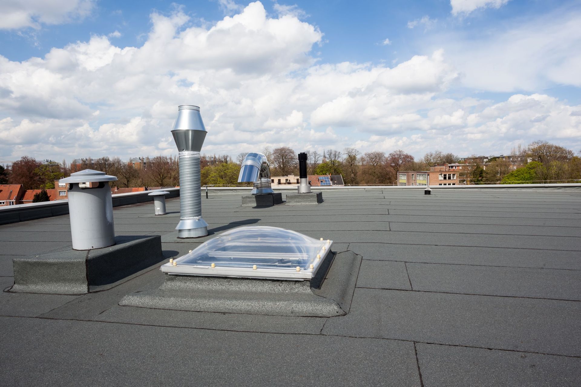 Flat rooftop with vent pipes and a skylight under a cloudy sky