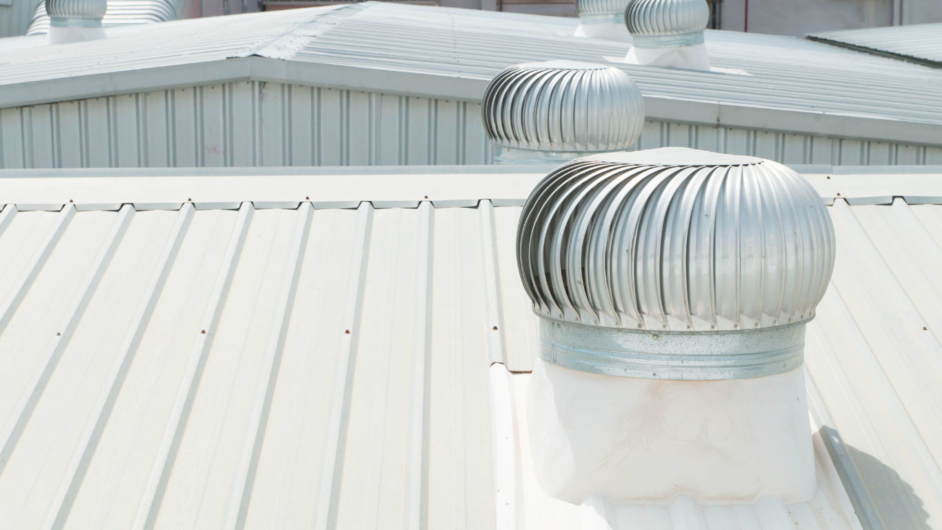 Rooftop with two silver turbine vents on a white metal roof under bright sunlight