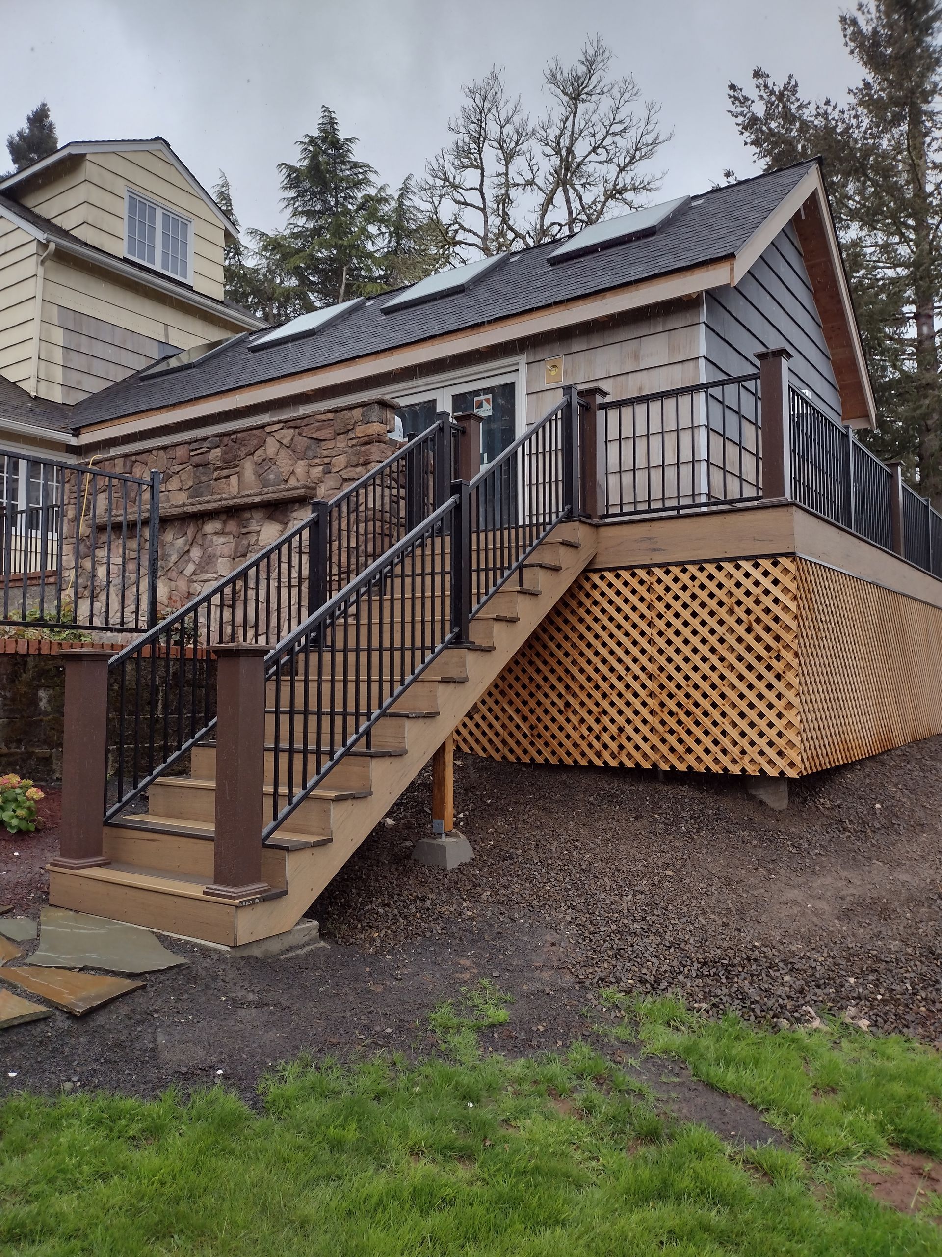 Exterior staircase leading to a raised house with black railings and tan siding, on a gravel yard.
