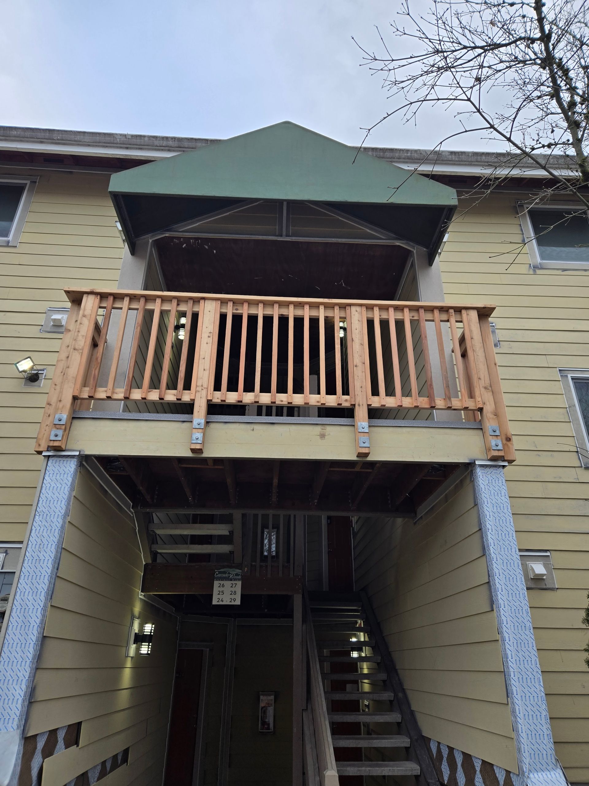 Apartment entrance with wooden balcony, green awning, and exterior stairs below
