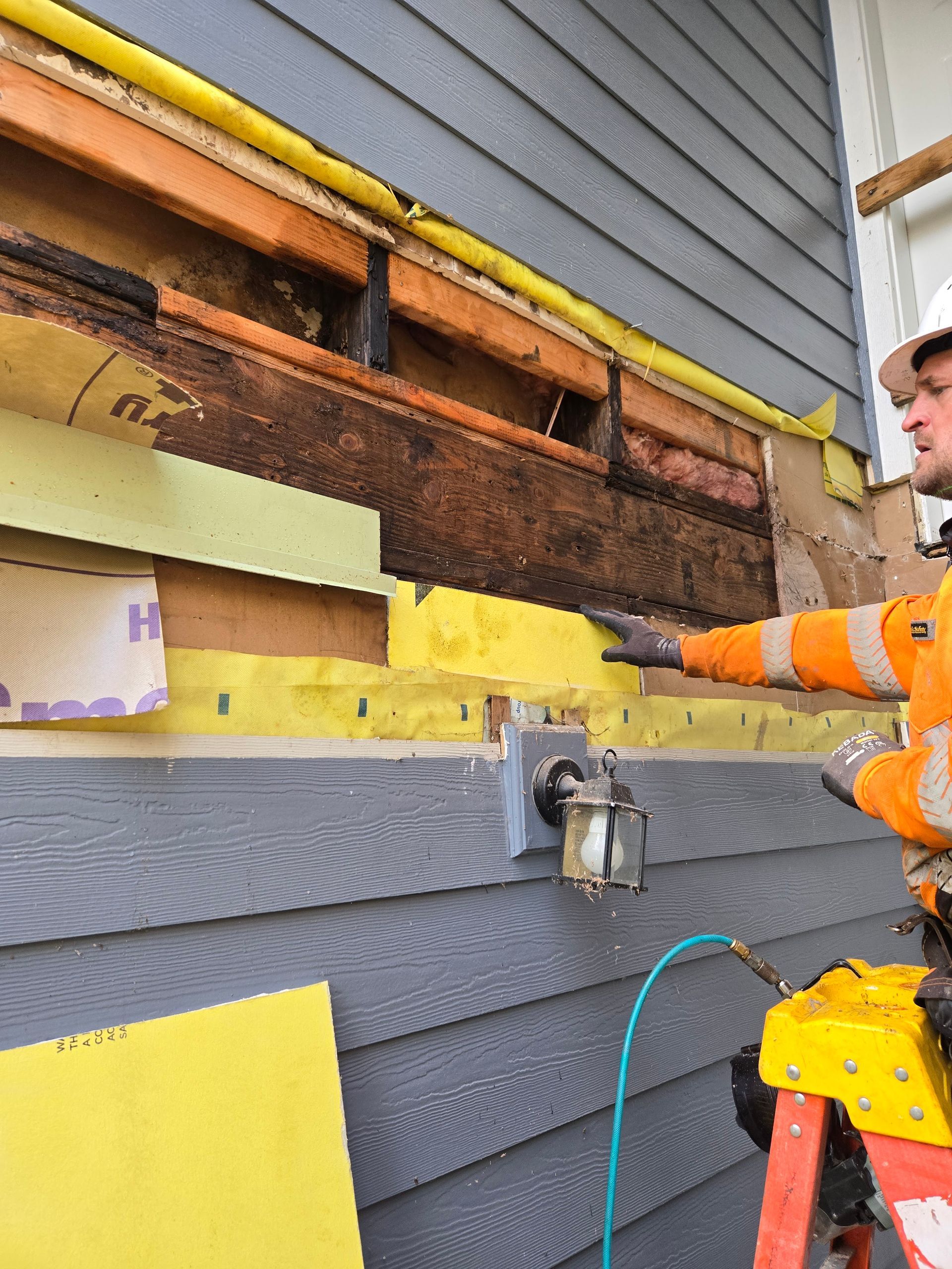 Worker in orange jacket repairs exterior wall siding with exposed insulation.