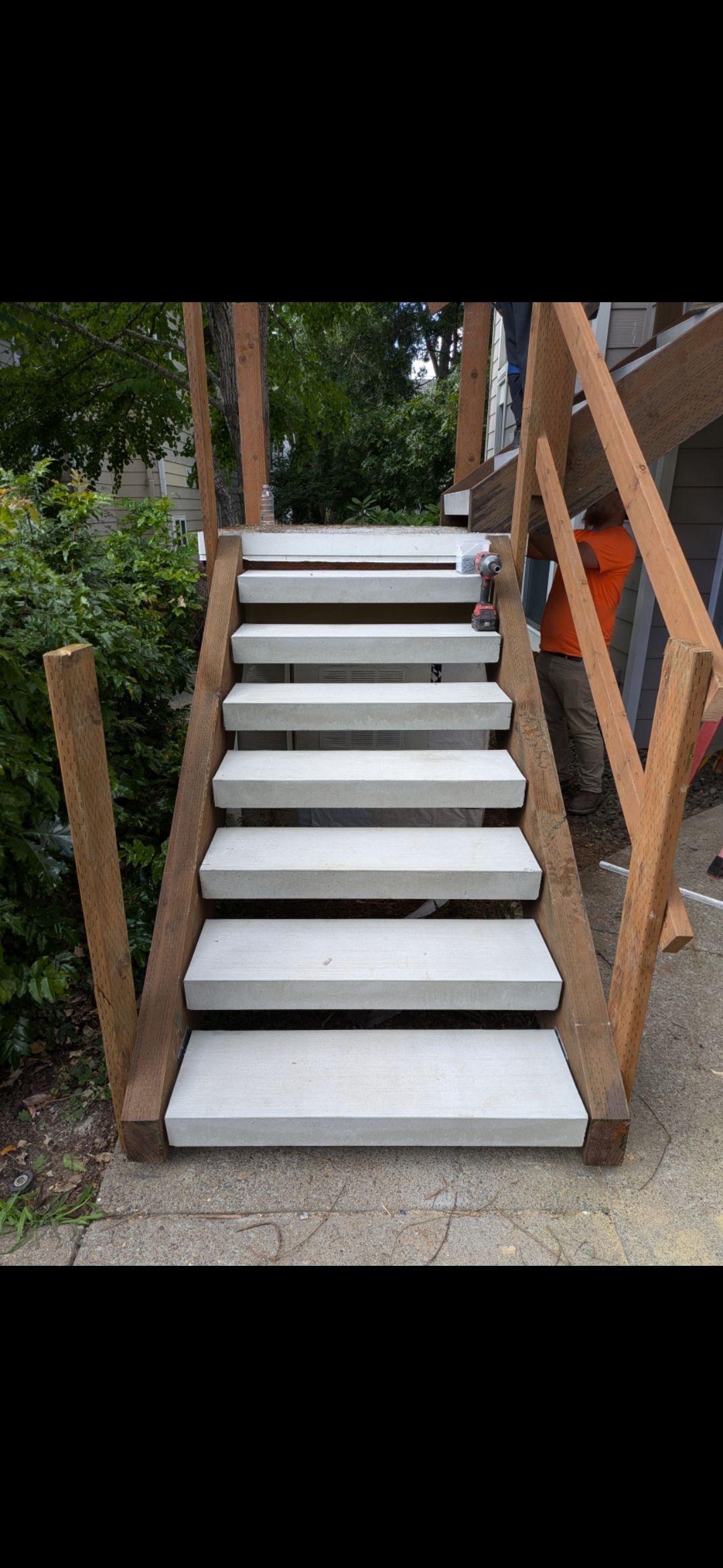 Outdoor wooden staircase with white steps and railings, leading up from a paved path.