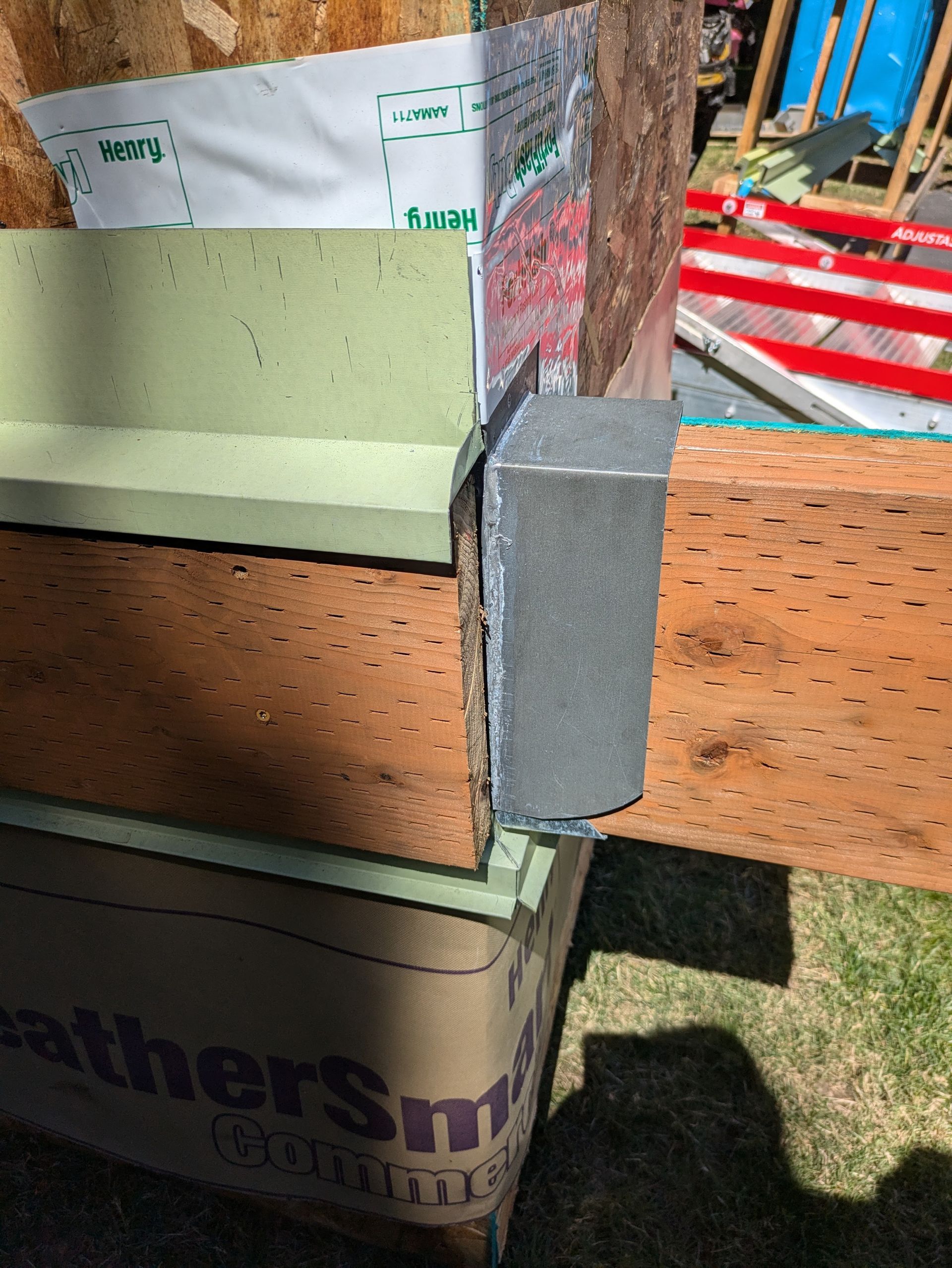 Close-up of a construction wall corner with wood framing, green foam board, and a metal bracket.