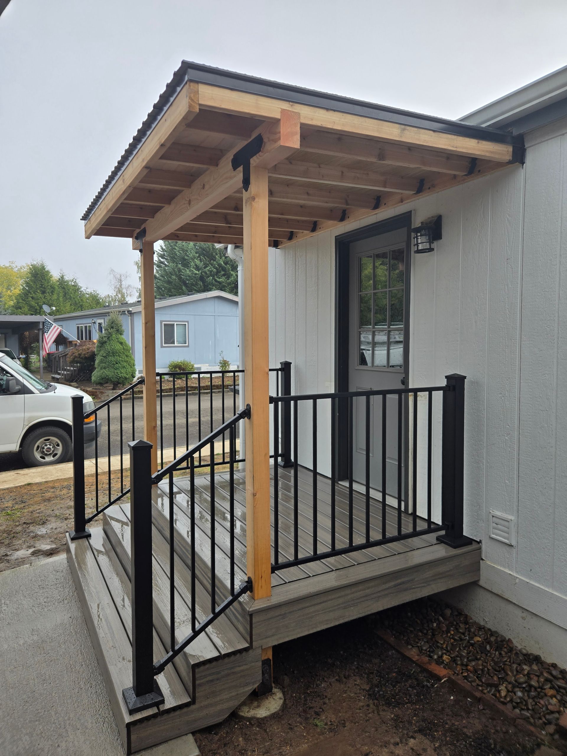 Small porch with steps, black railings, and a wooden awning on a house exterior.