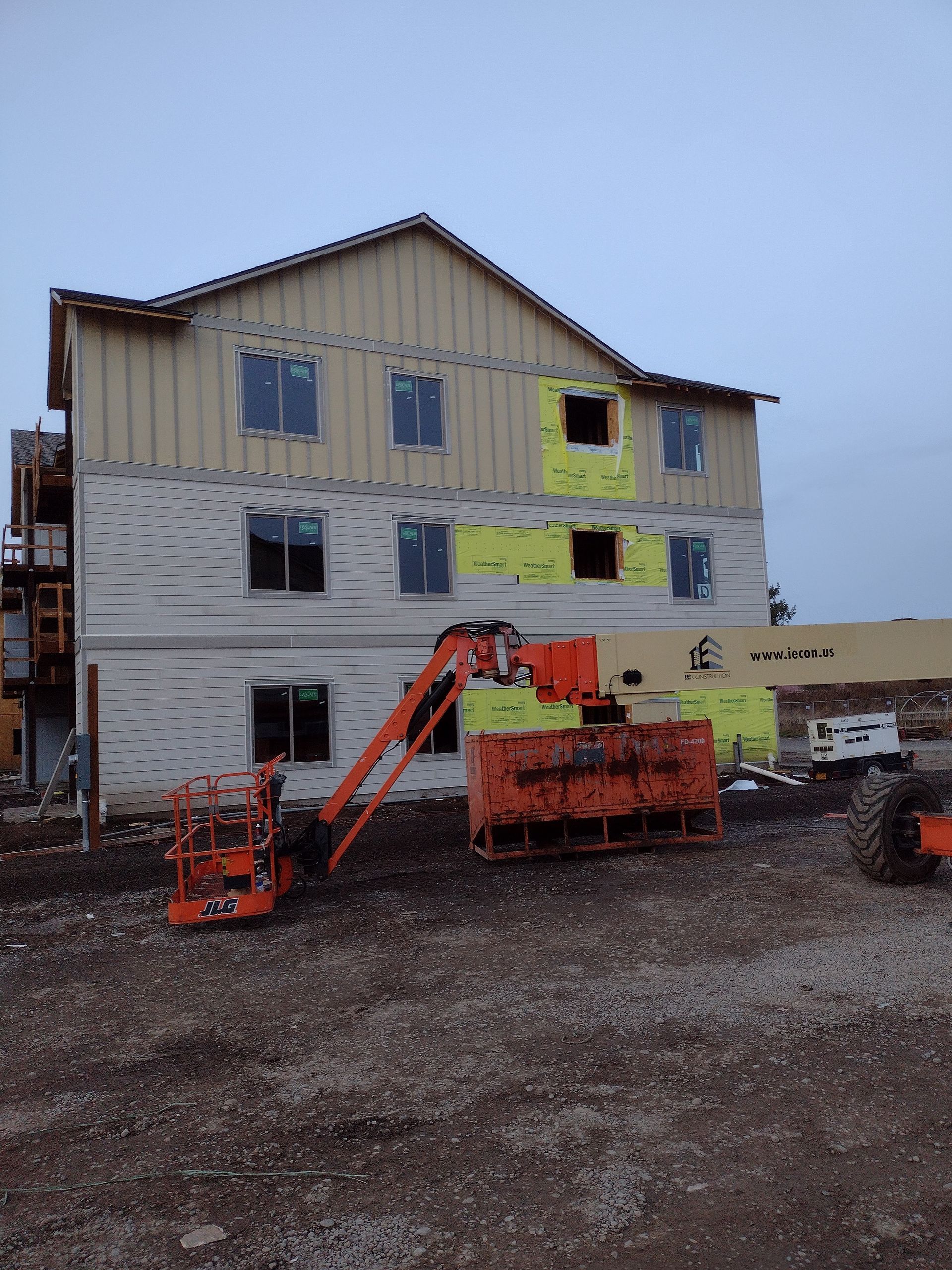 Two-story house under construction with lift equipment and gravel lot in front