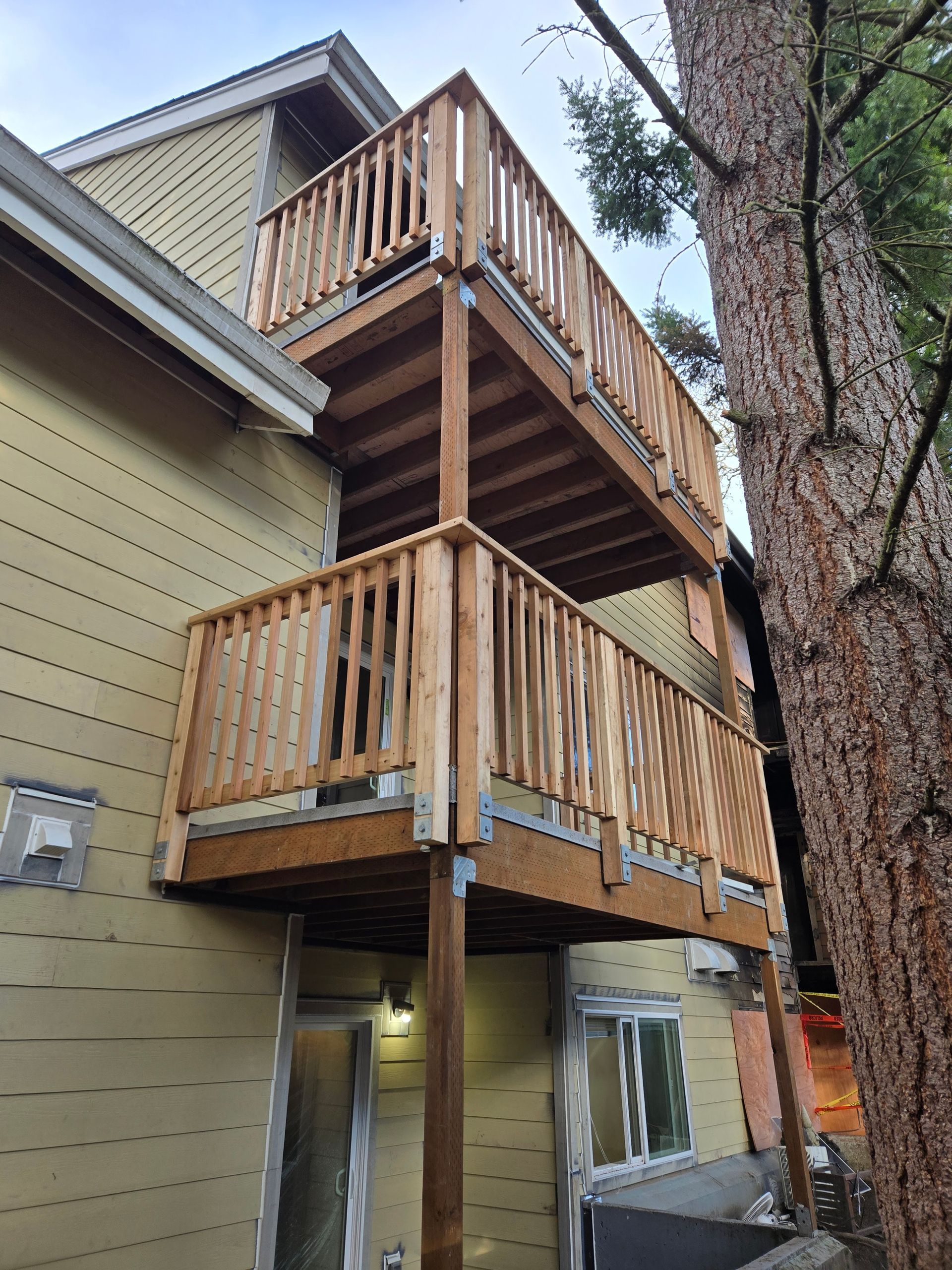 Two stacked wooden balconies attached to a beige house beside a large tree