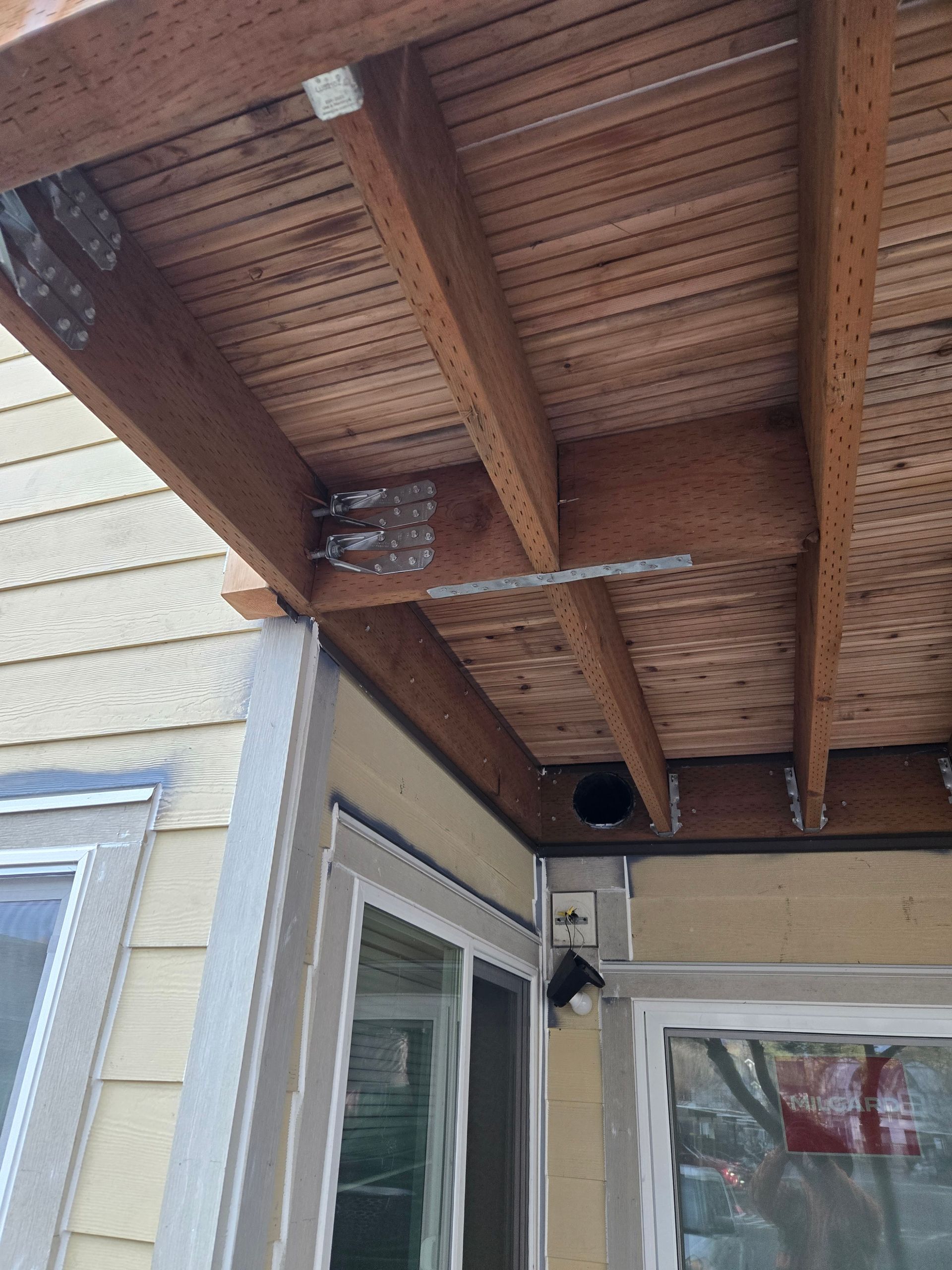Underside of a wooden porch roof with beams and metal brackets above a doorway