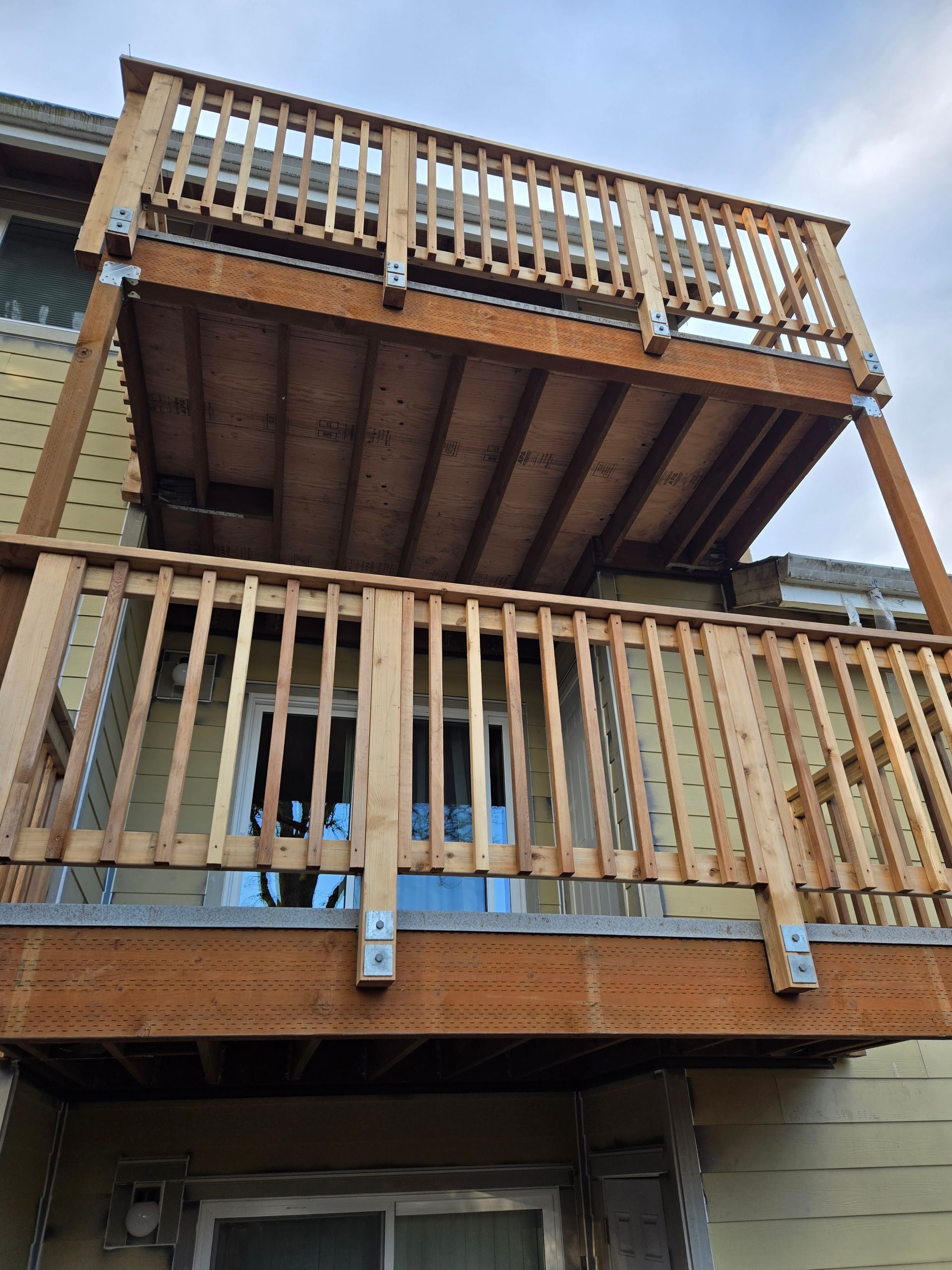 Wooden deck and railing under construction above a garage, viewed from below