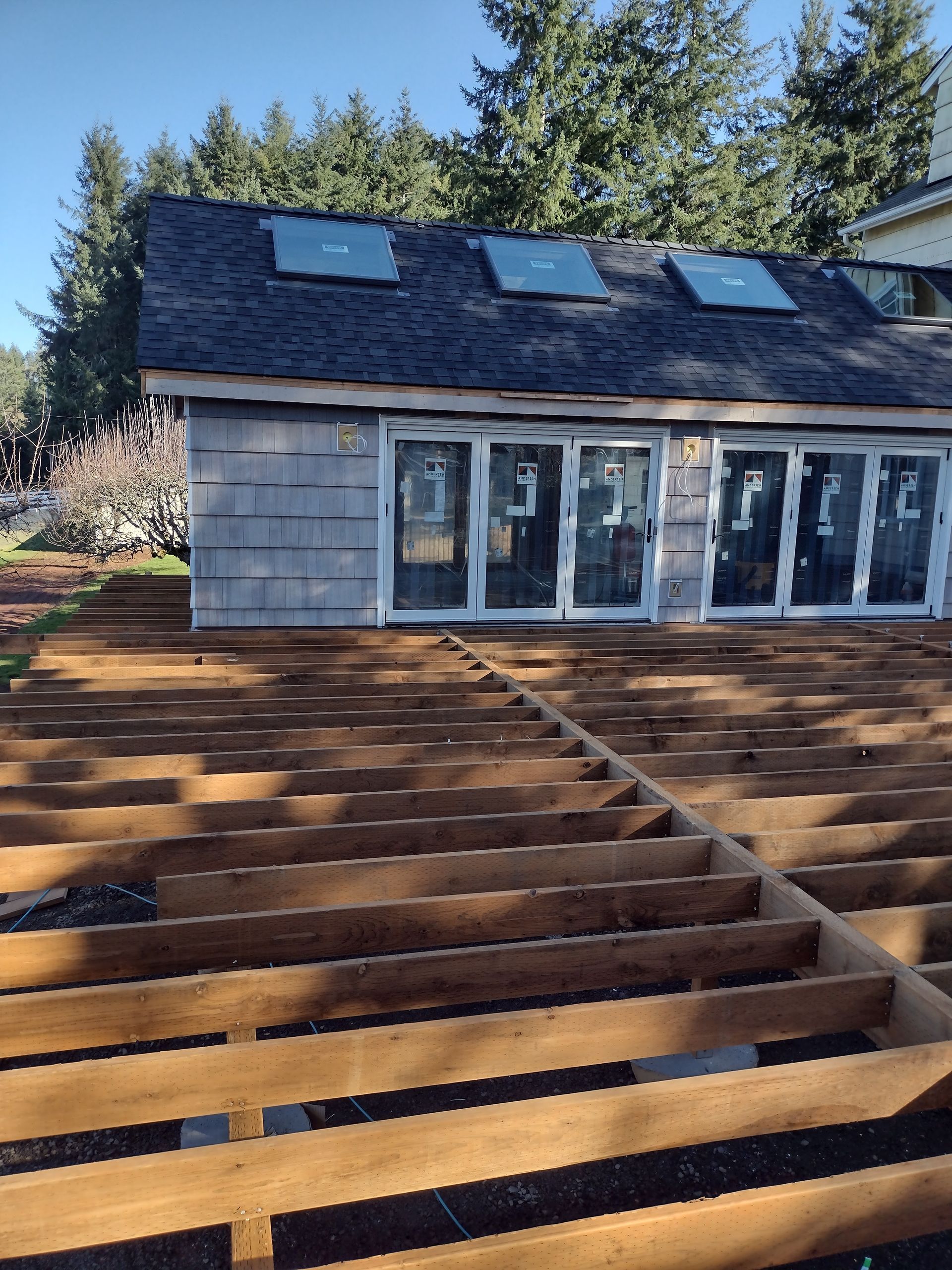 Wooden deck framing in front of a gray house with skylights and glass doors