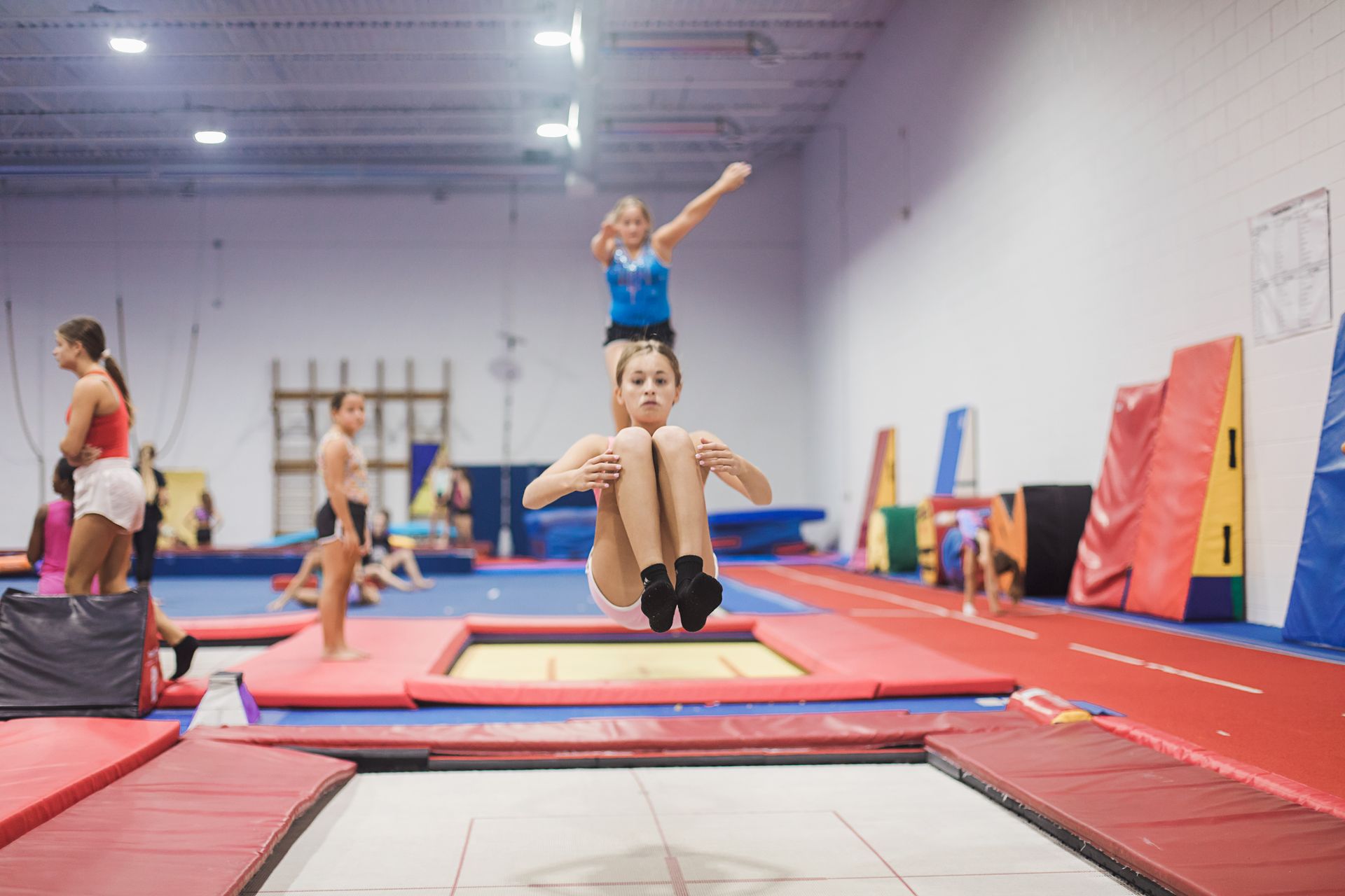 A woman is jumping on a trampoline in a gym.