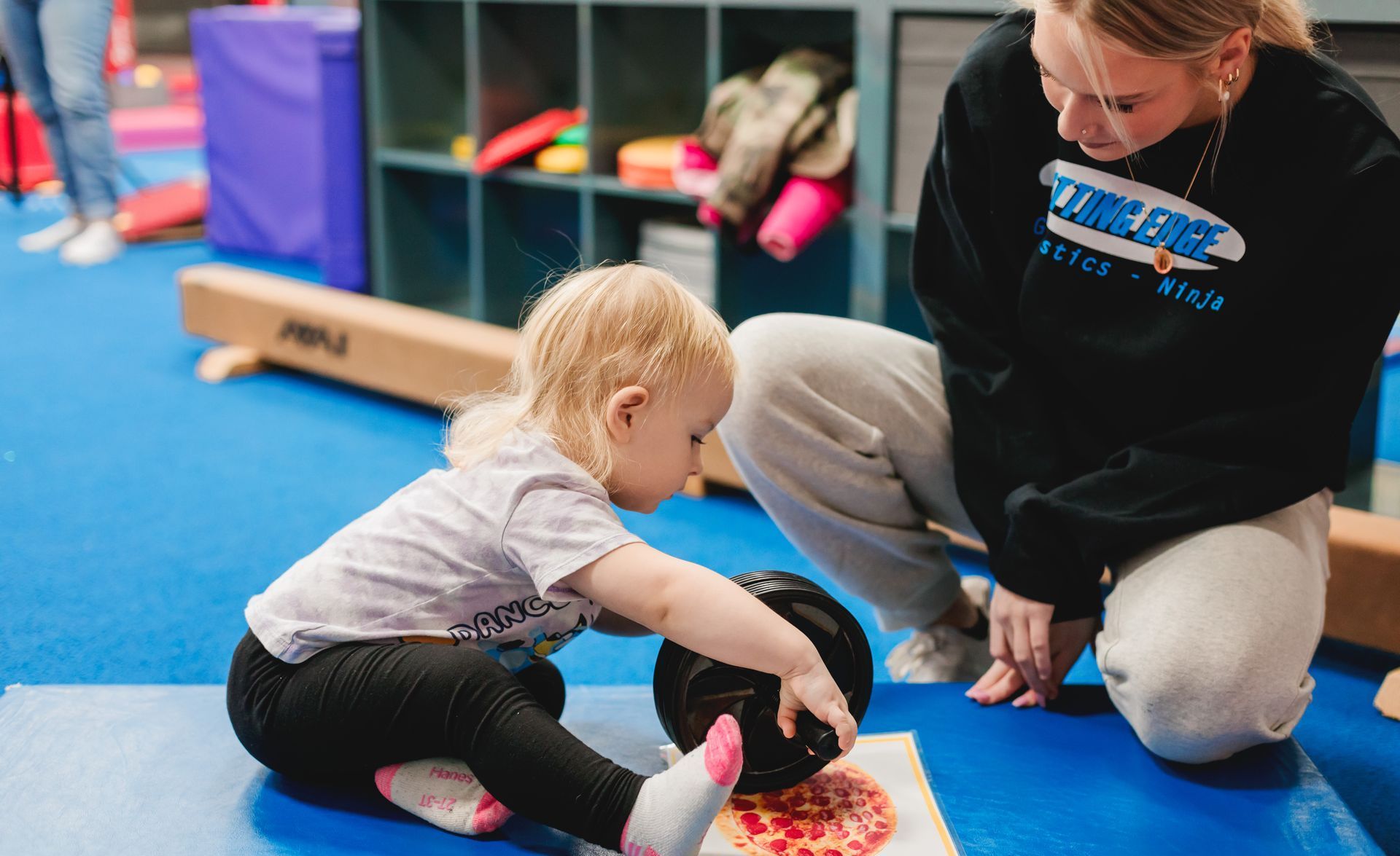 A woman is kneeling down next to a little girl playing with a ball.