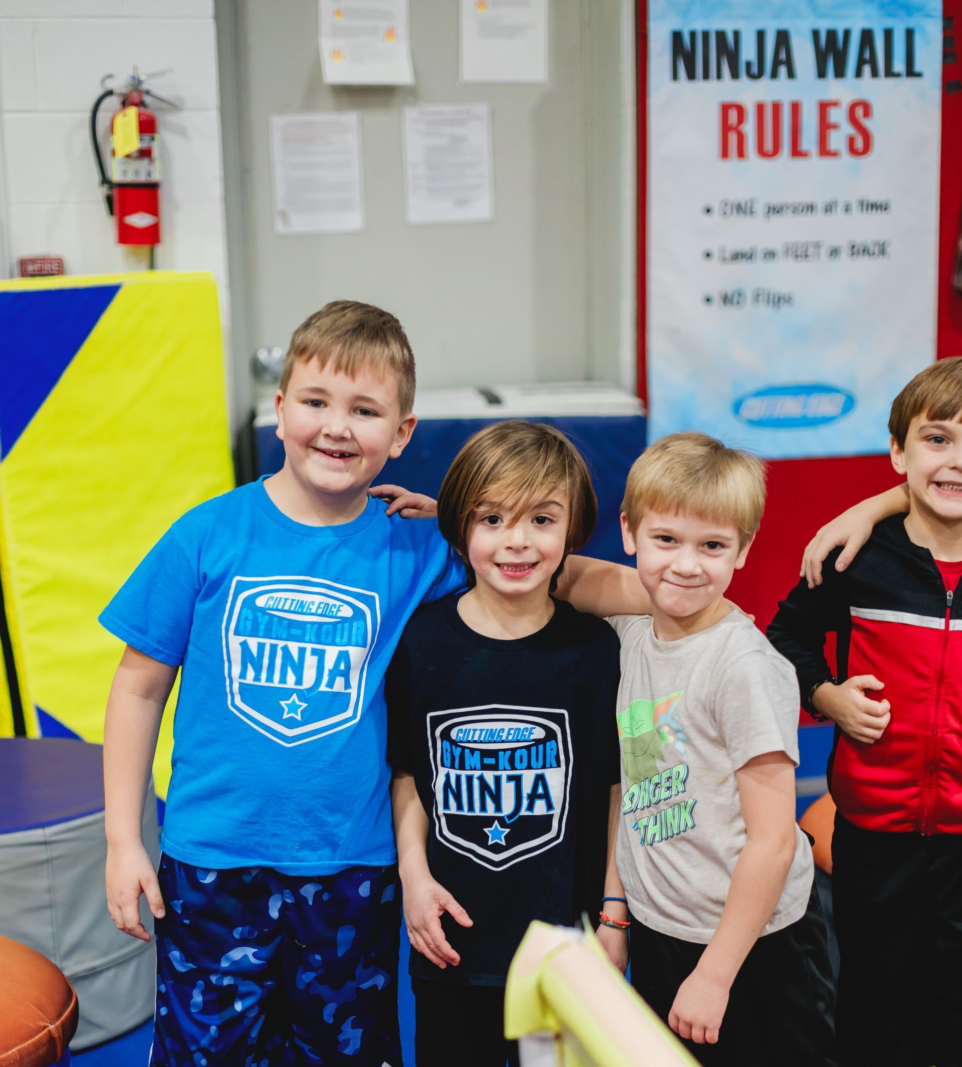 A group of young boys are posing for a picture in front of a sign that says ninja wall rules