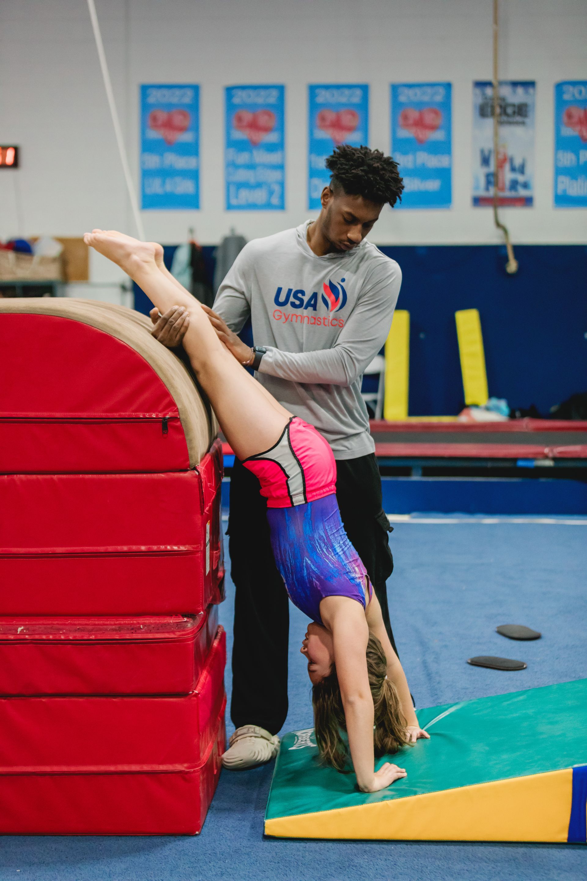 A man is helping a young girl do a handstand on a gymnastics mat.