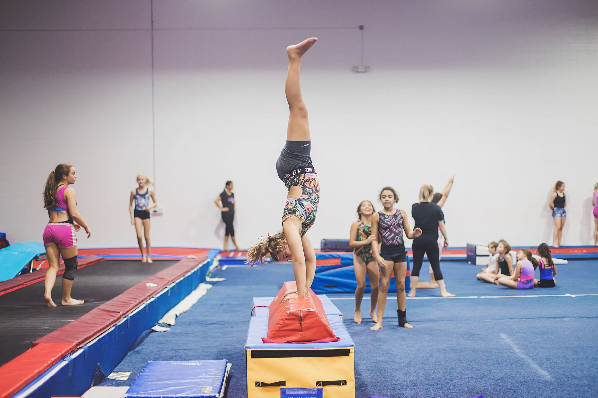A girl is doing a handstand on a box in a gym.
