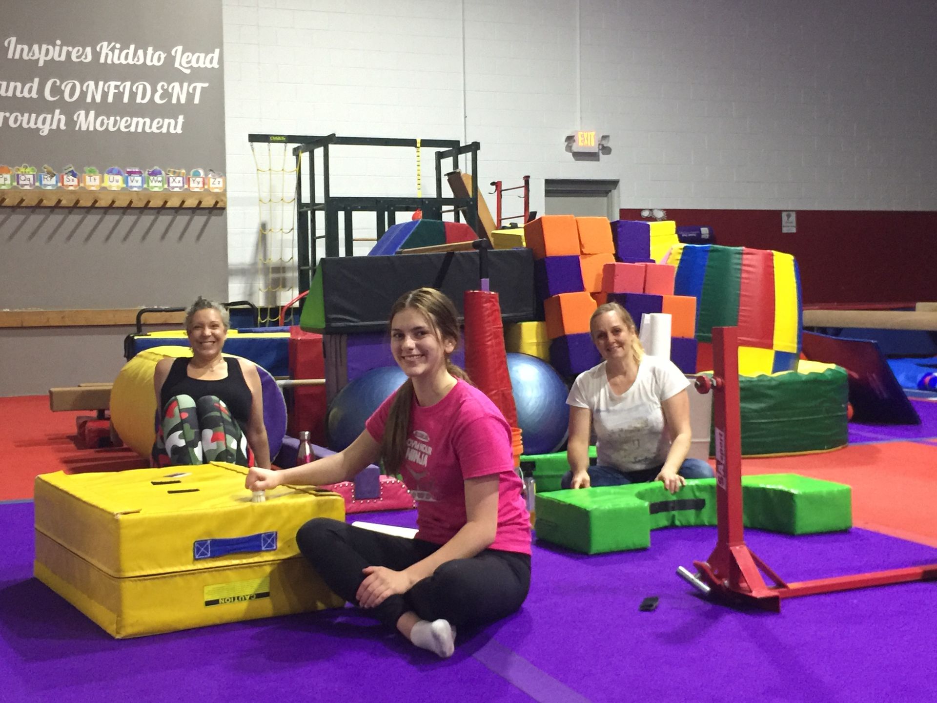 A group of women are sitting on the floor in a gym.