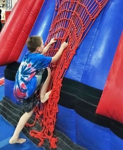A young boy is climbing up a red net on a bouncy house.