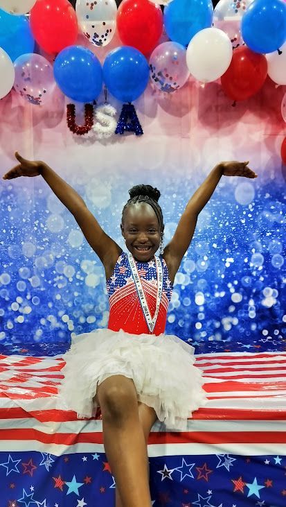 A young girl is sitting on a table with her arms outstretched in front of balloons.