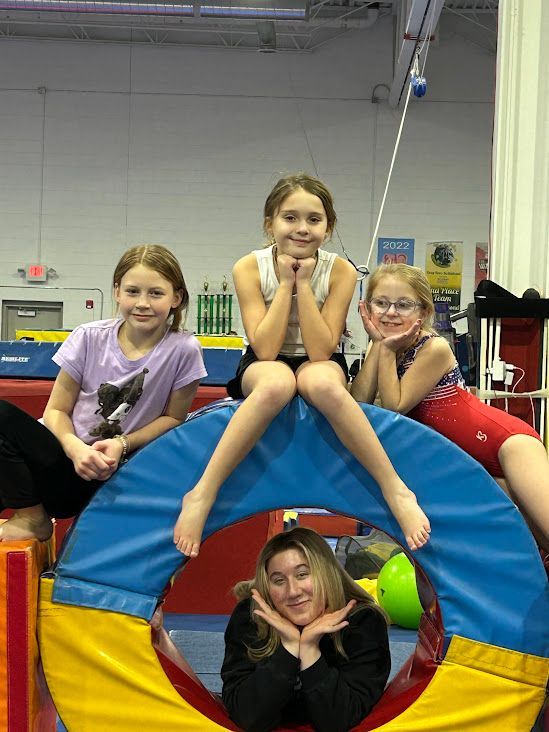 A group of young girls are sitting on a foam ring in a gym.