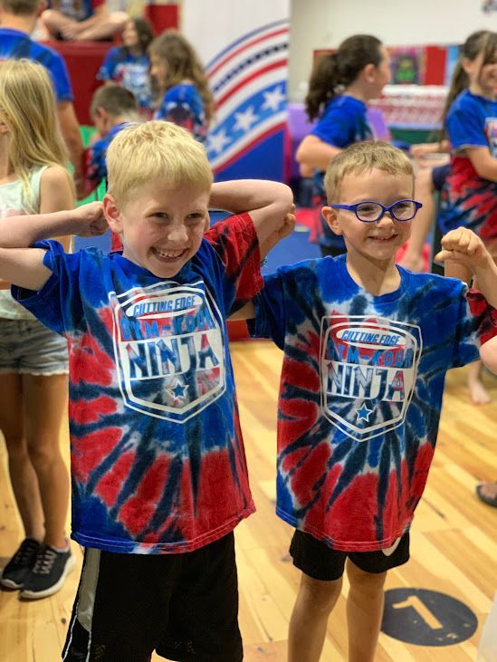 Two young boys wearing tie dye shirts are standing next to each other in a gym.