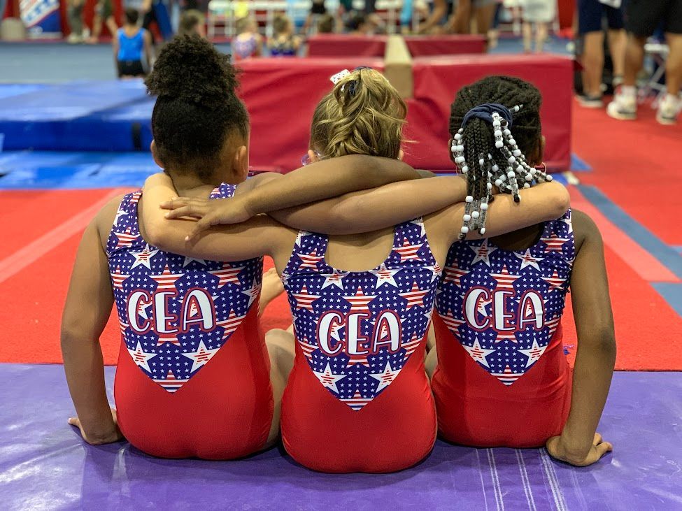 Three young girls are sitting on the floor with their arms around each other.