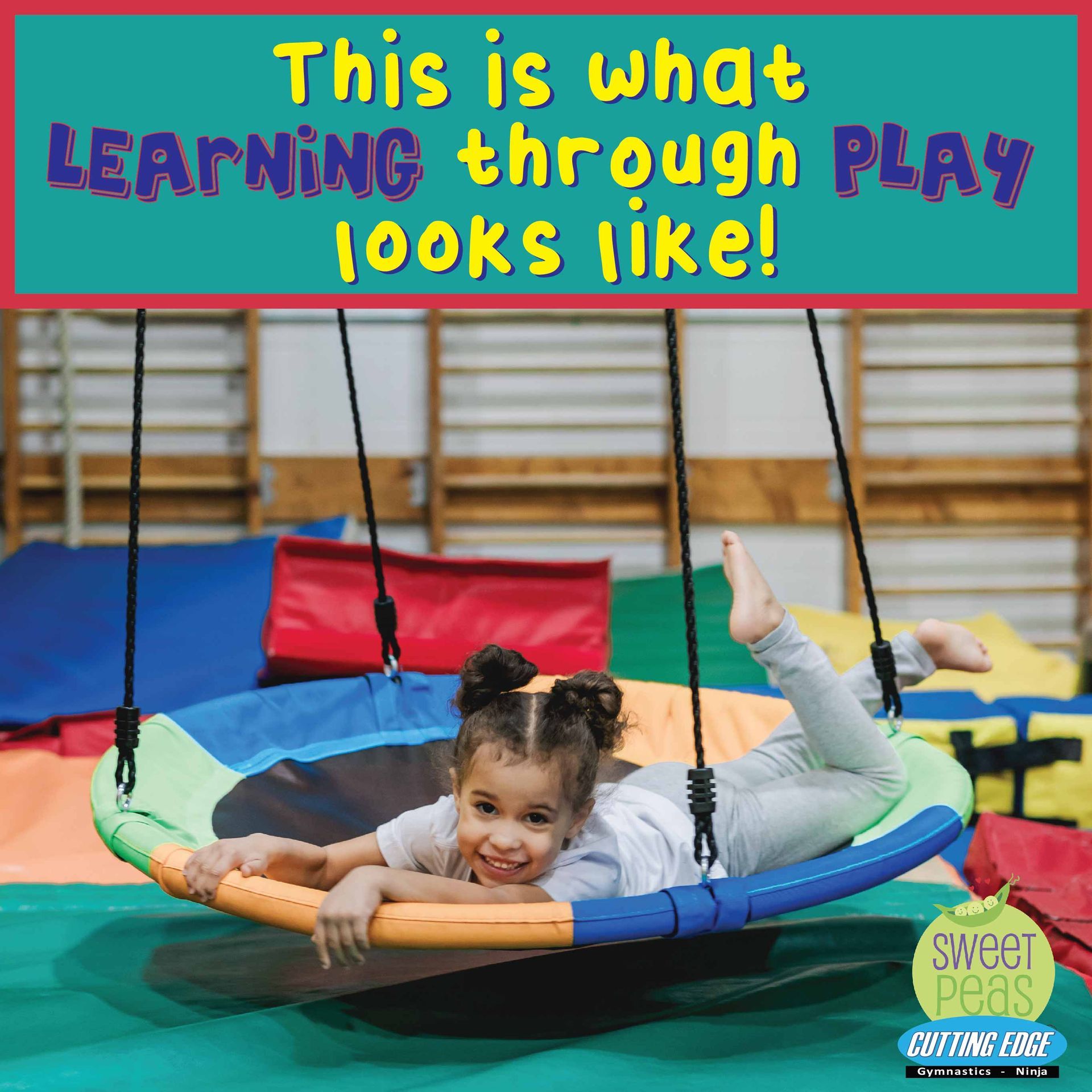 A little girl is laying on a swing in a gym.
