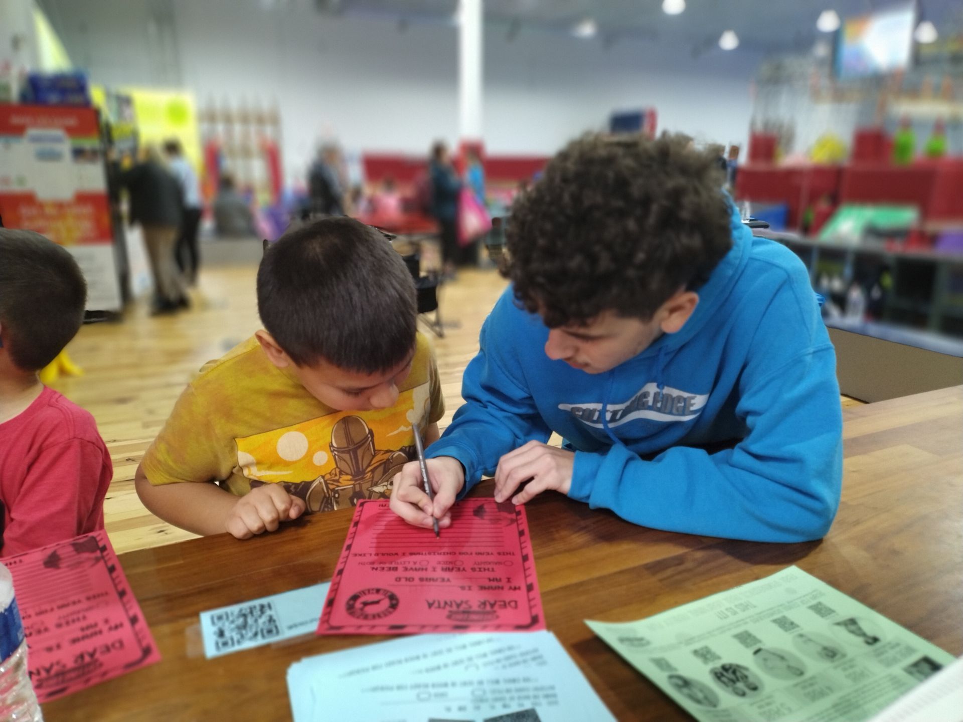 Two young boys are sitting at a table writing on a piece of paper.