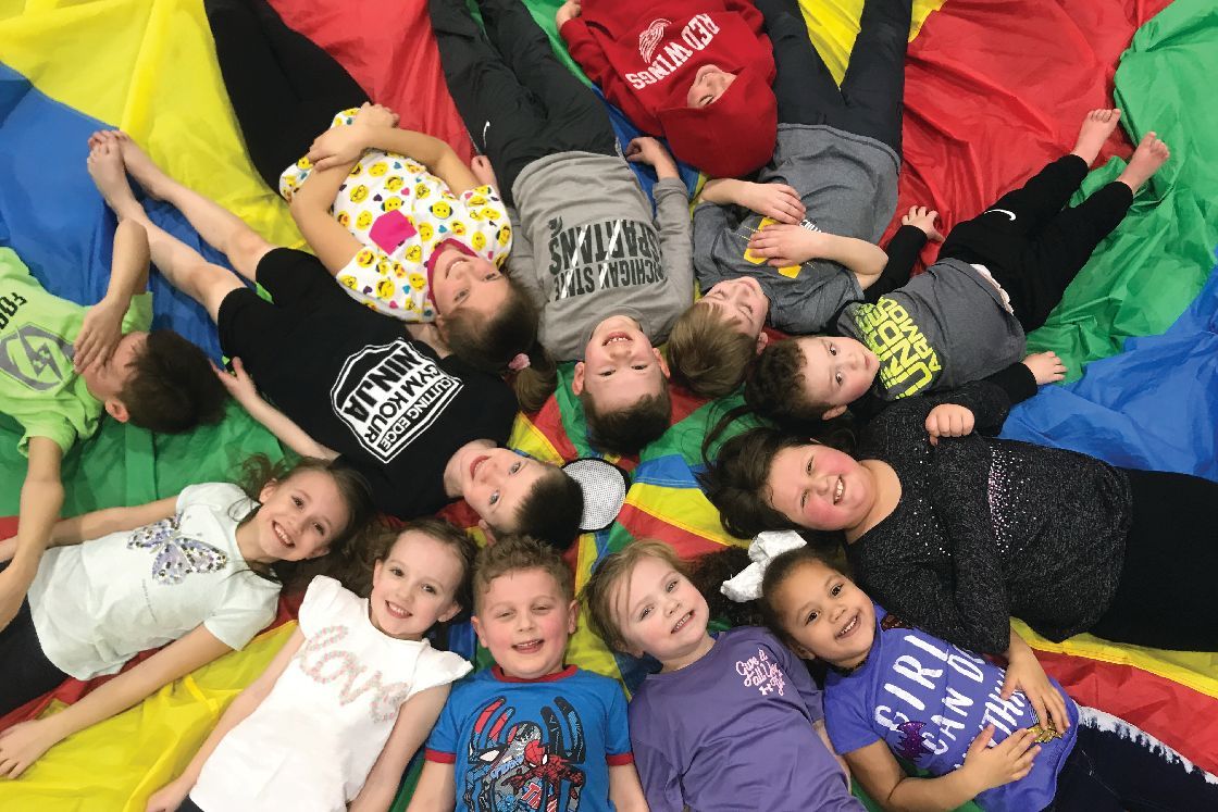 A group of children are laying in a circle on a colorful parachute.