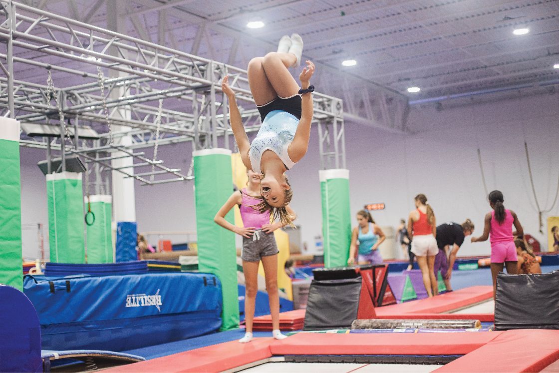 A girl is doing a handstand on a trampoline in a gym.