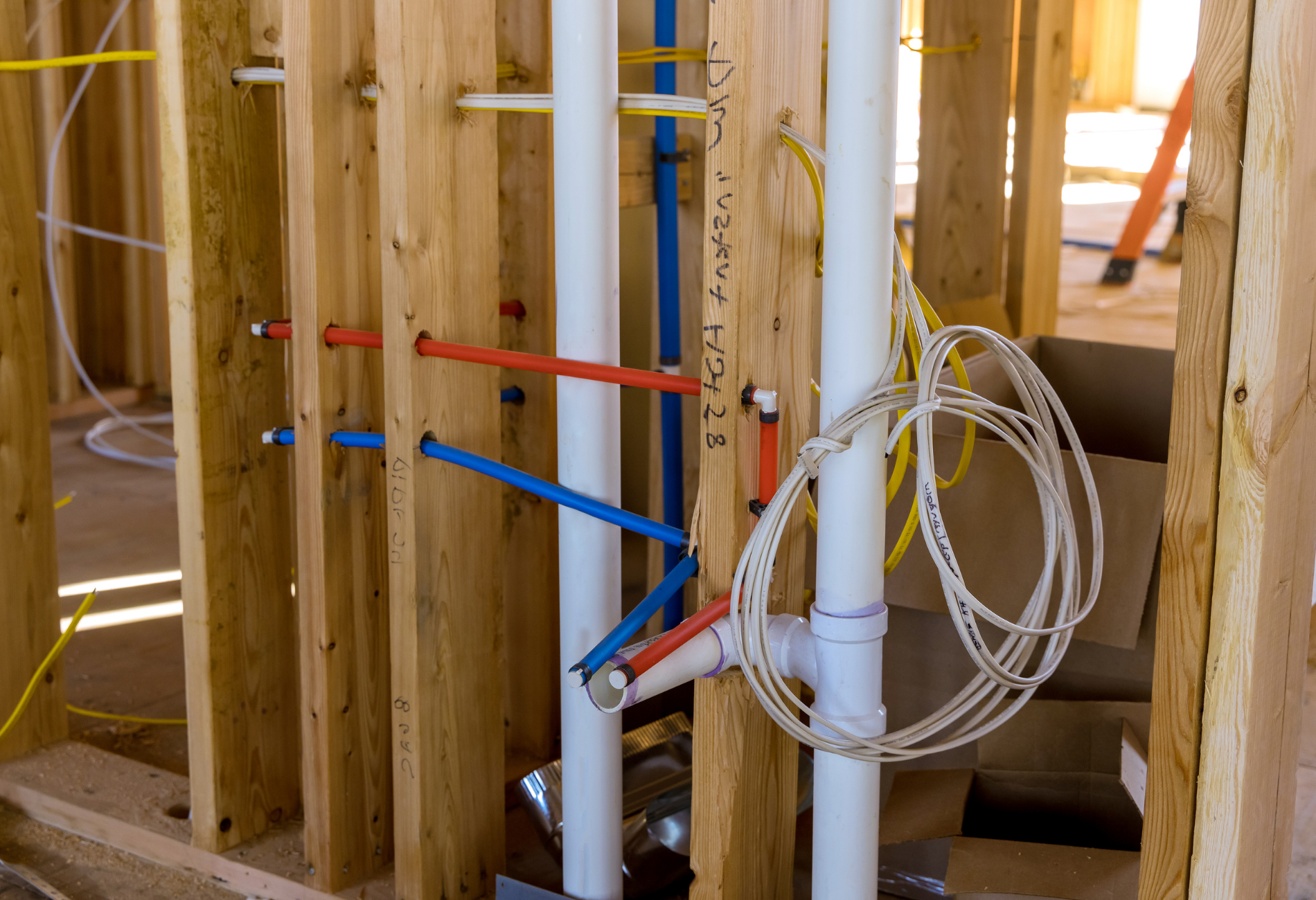 Framing with plumbing and electrical wiring in a construction site. Blue, red, and white pipes with yellow wires.