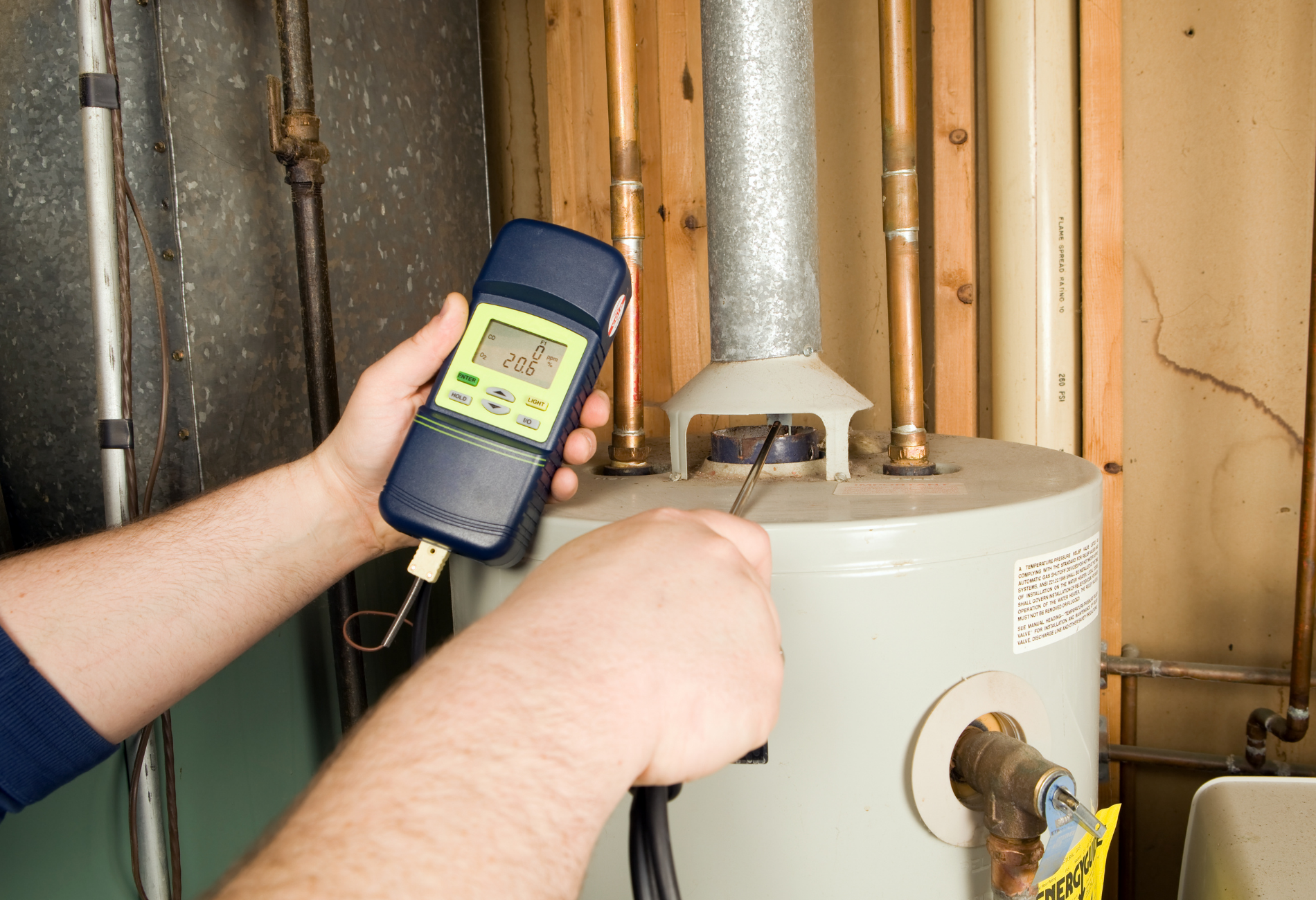 Person using a digital meter to check a water heater in a utility room.