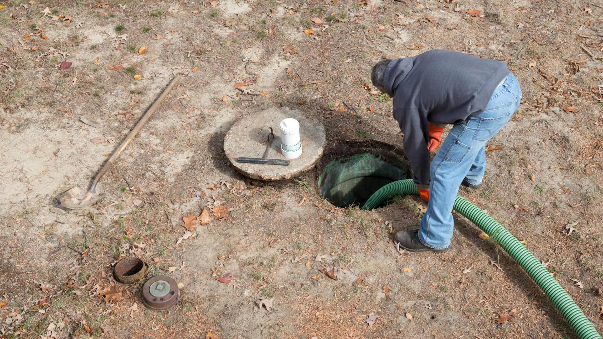 A man is pumping water into a septic tank with a green hose.